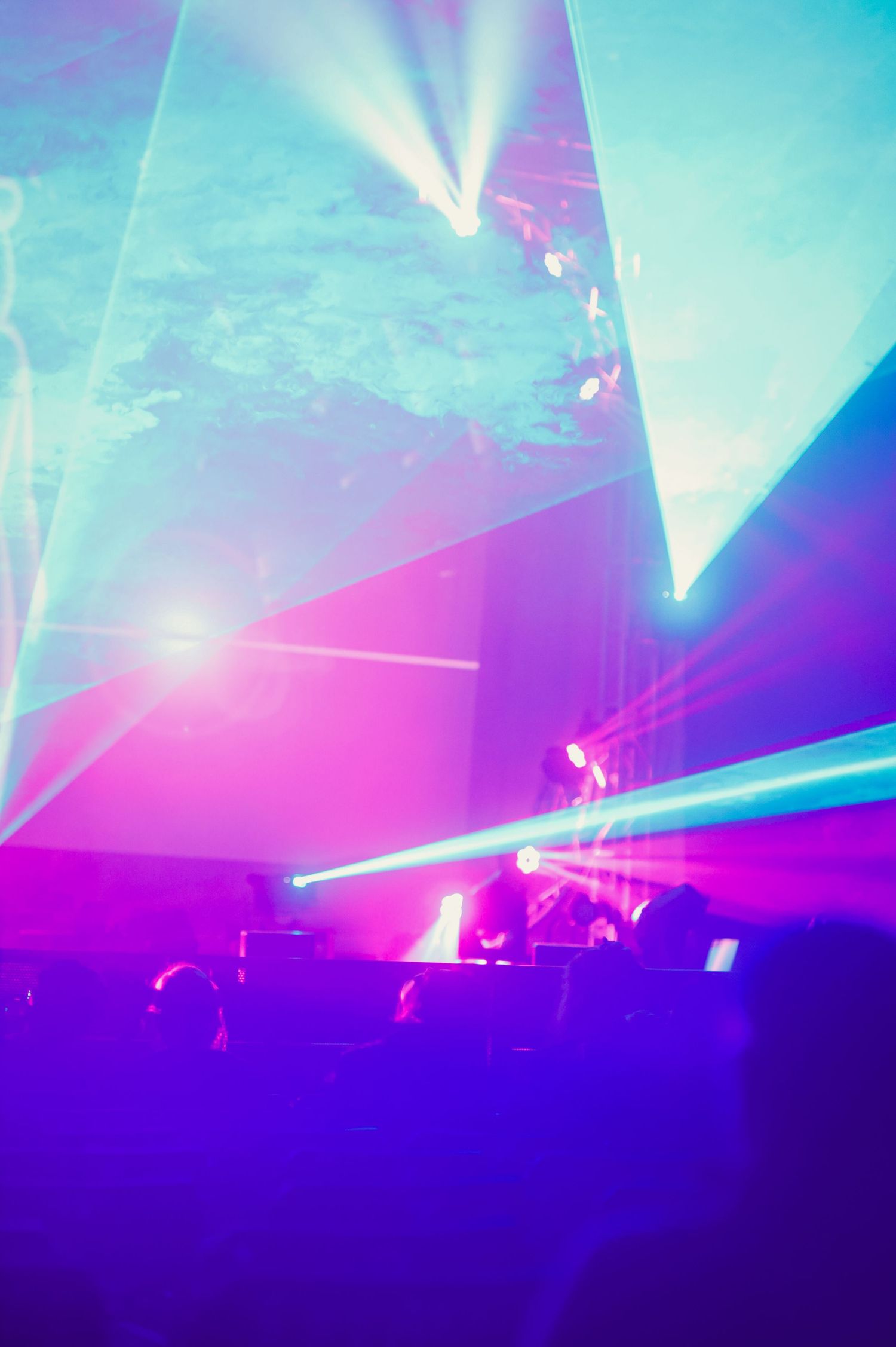 Vibrant laser light show illuminates a nightclub performance with pink and blue beams cutting through smoke-filled air.