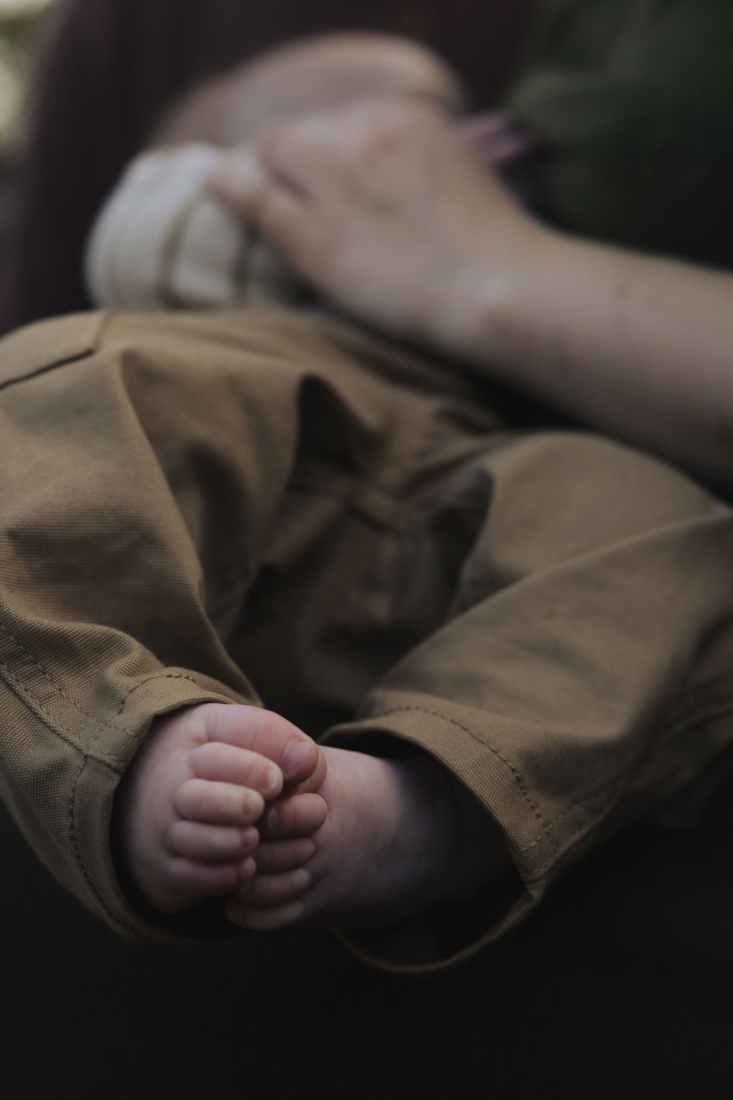 Close-up view of tiny baby feet peeking out from brown fabric clothing in soft natural lighting.