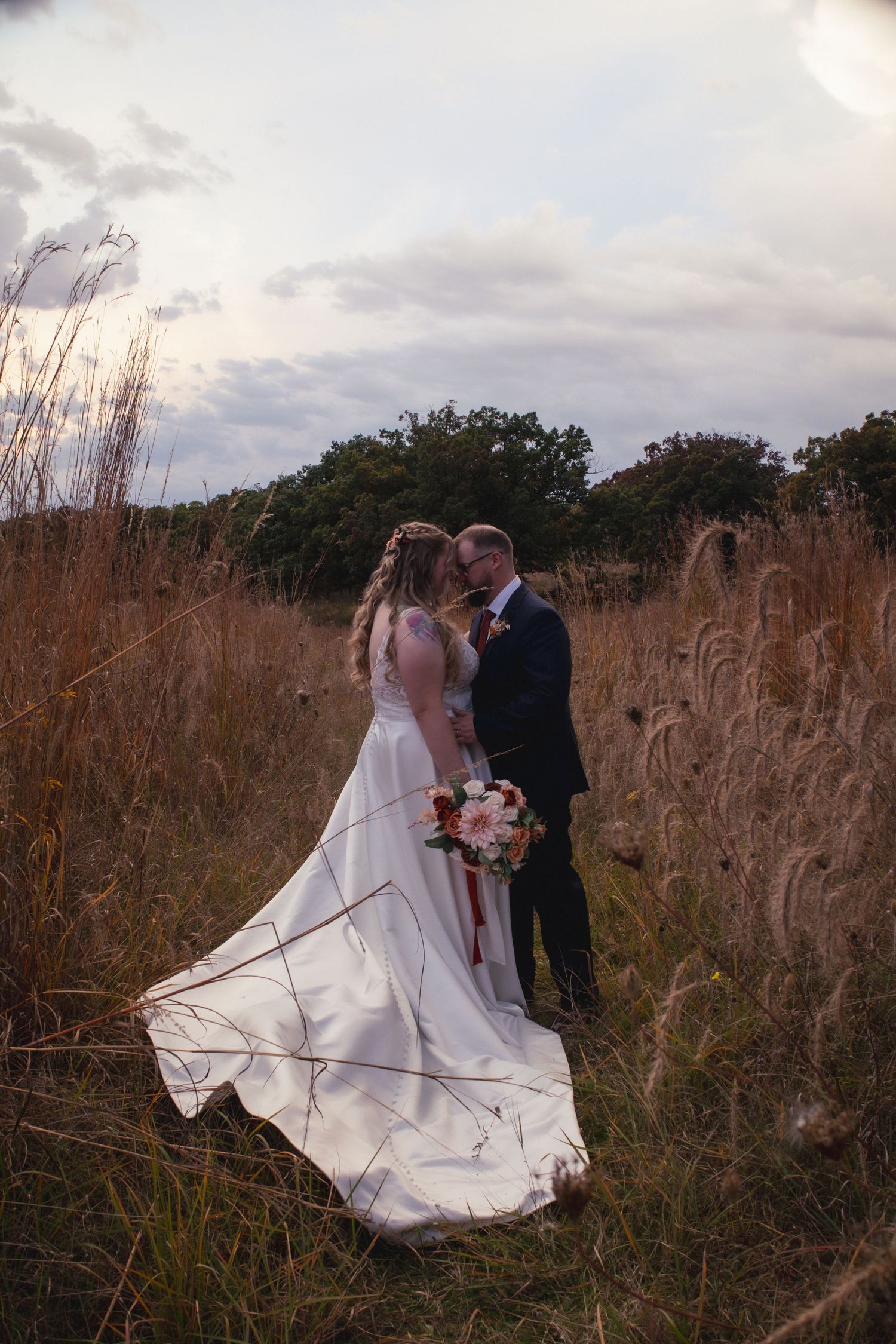 Wedding couple standing in tall autumn grass during golden hour photography session.