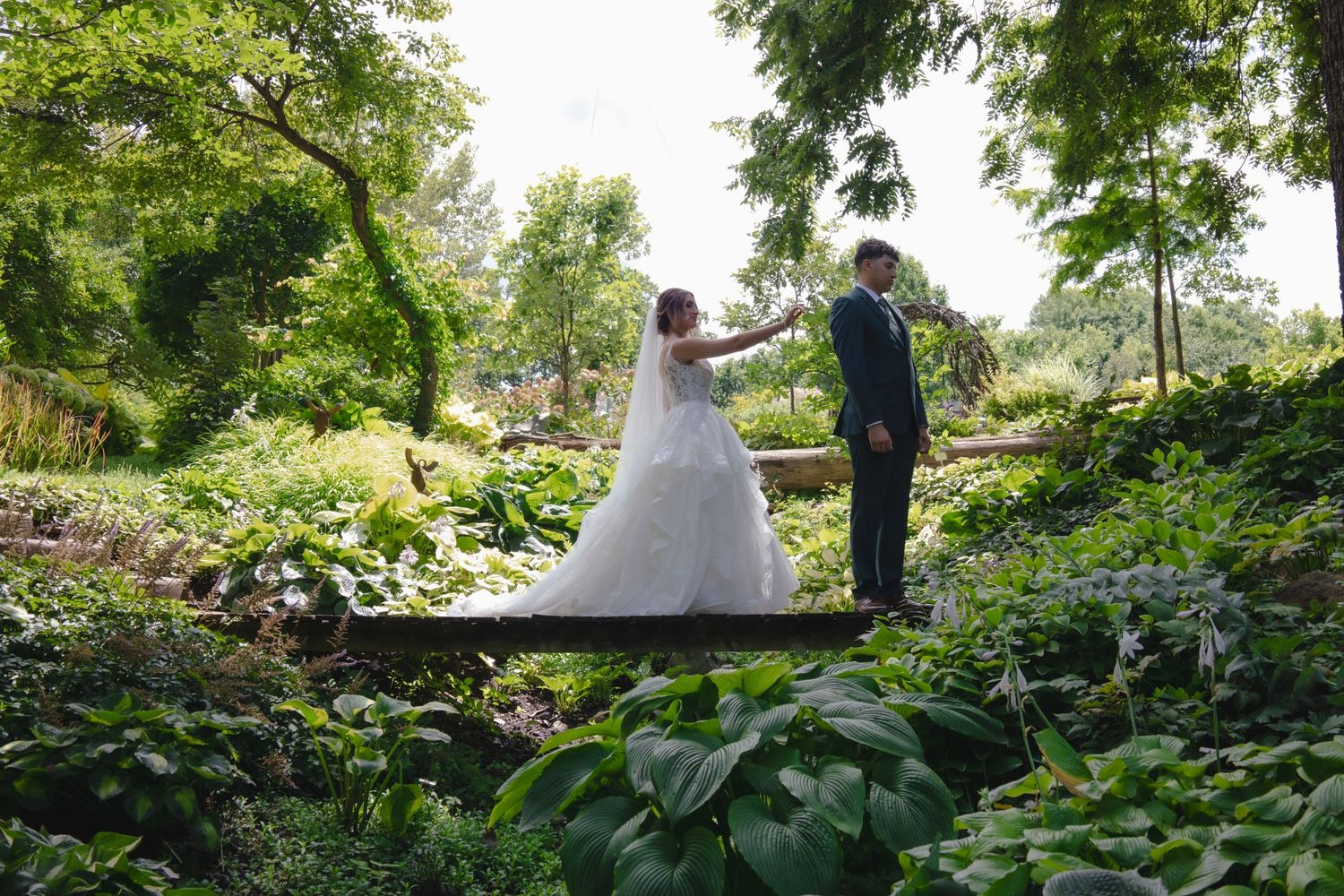 Wedding couple standing on garden bridge surrounded by lush greenery.