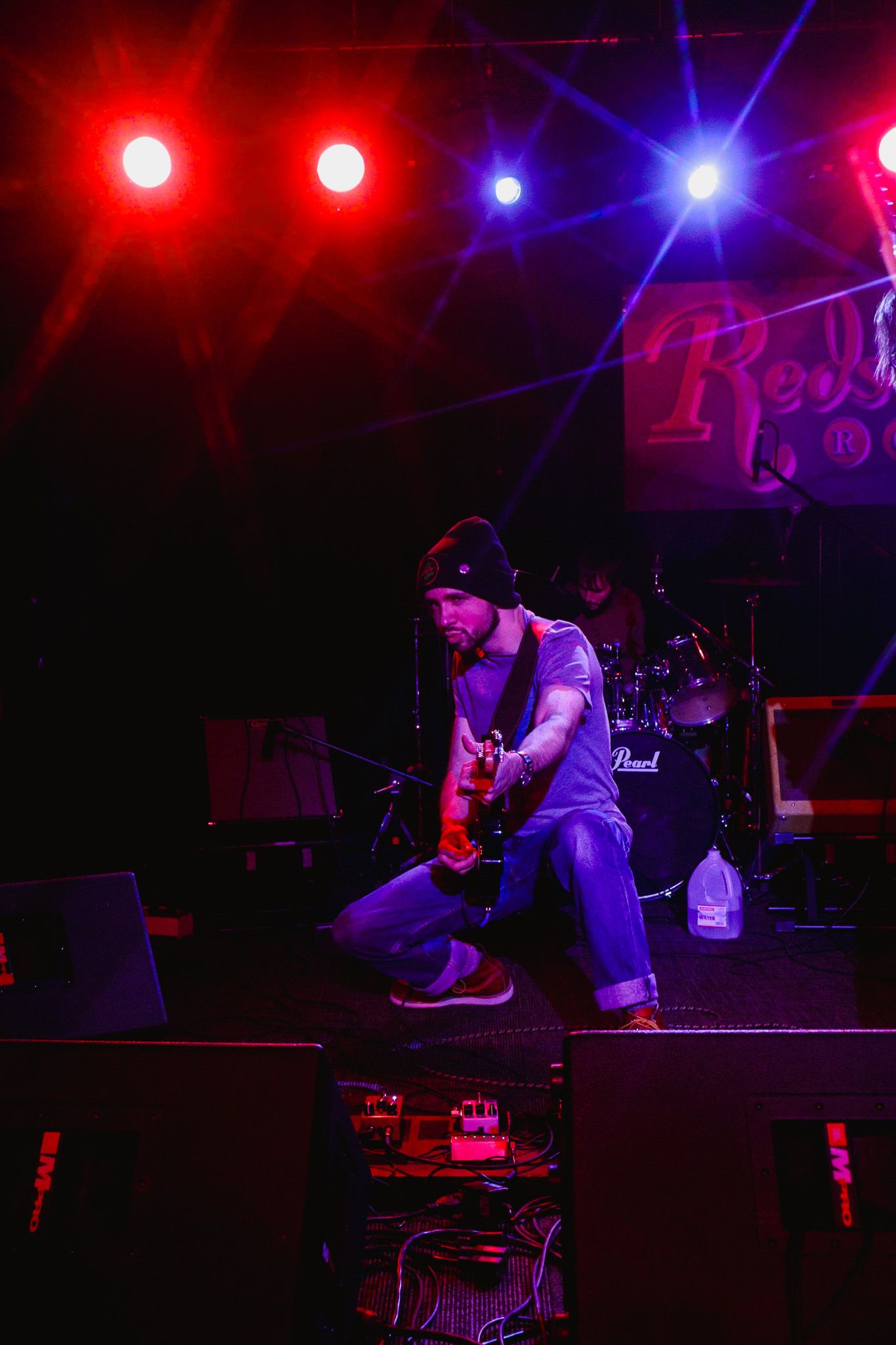 Guitarist performs on stage under dramatic red and blue concert lighting at a nightclub venue.