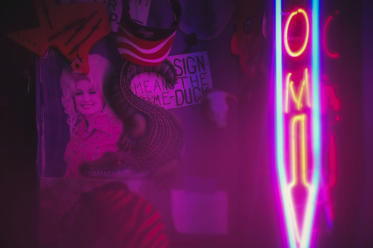 Neon pink OMY sign glows against a dark background with abstract wall art silhouettes.