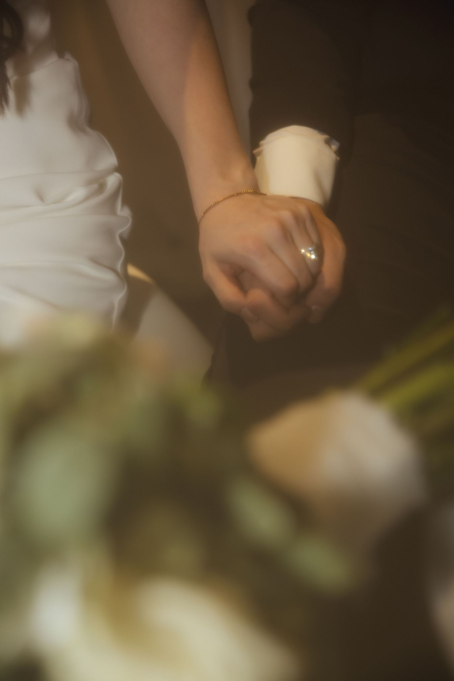 Soft focus close-up of a hand wearing a delicate engagement ring against a light, dreamy background.