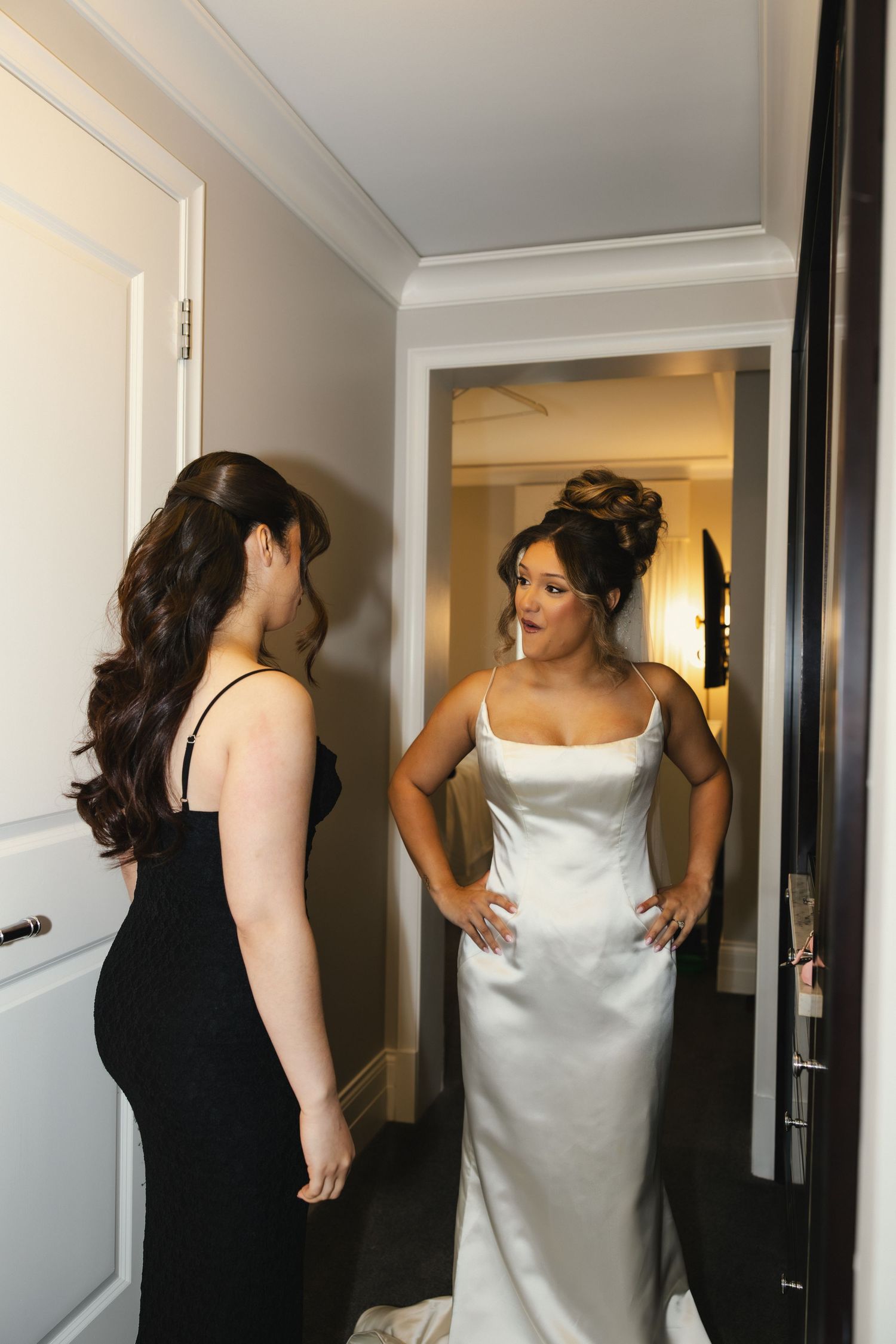 Women in formal attire help adjust a white wedding dress during pre-ceremony preparations.