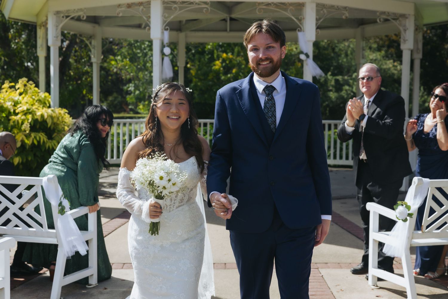 Wedding party poses together outdoors in front of white garden trellis with greenery and flowers in background.