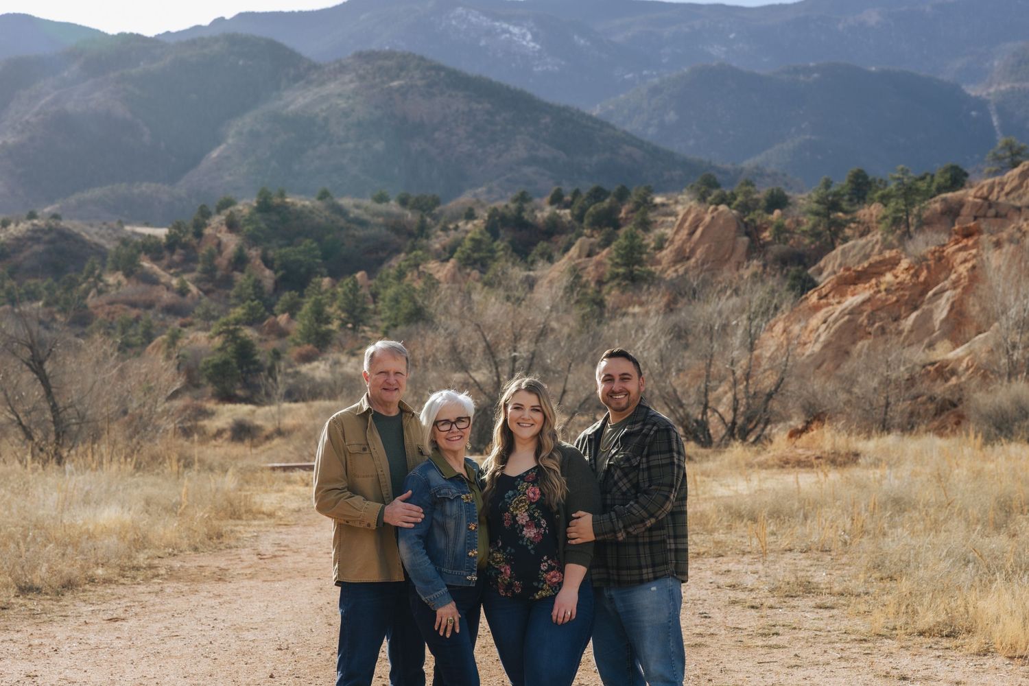 Family of four posing outdoors with Rocky Mountain landscape and red rock formations in background.