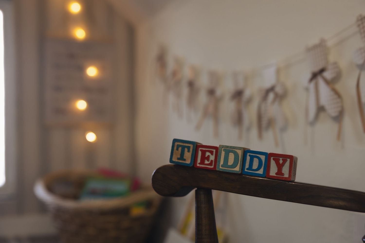 Colorful wooden alphabet blocks spelling TEDDY on a wooden stand in a softly lit nursery room.