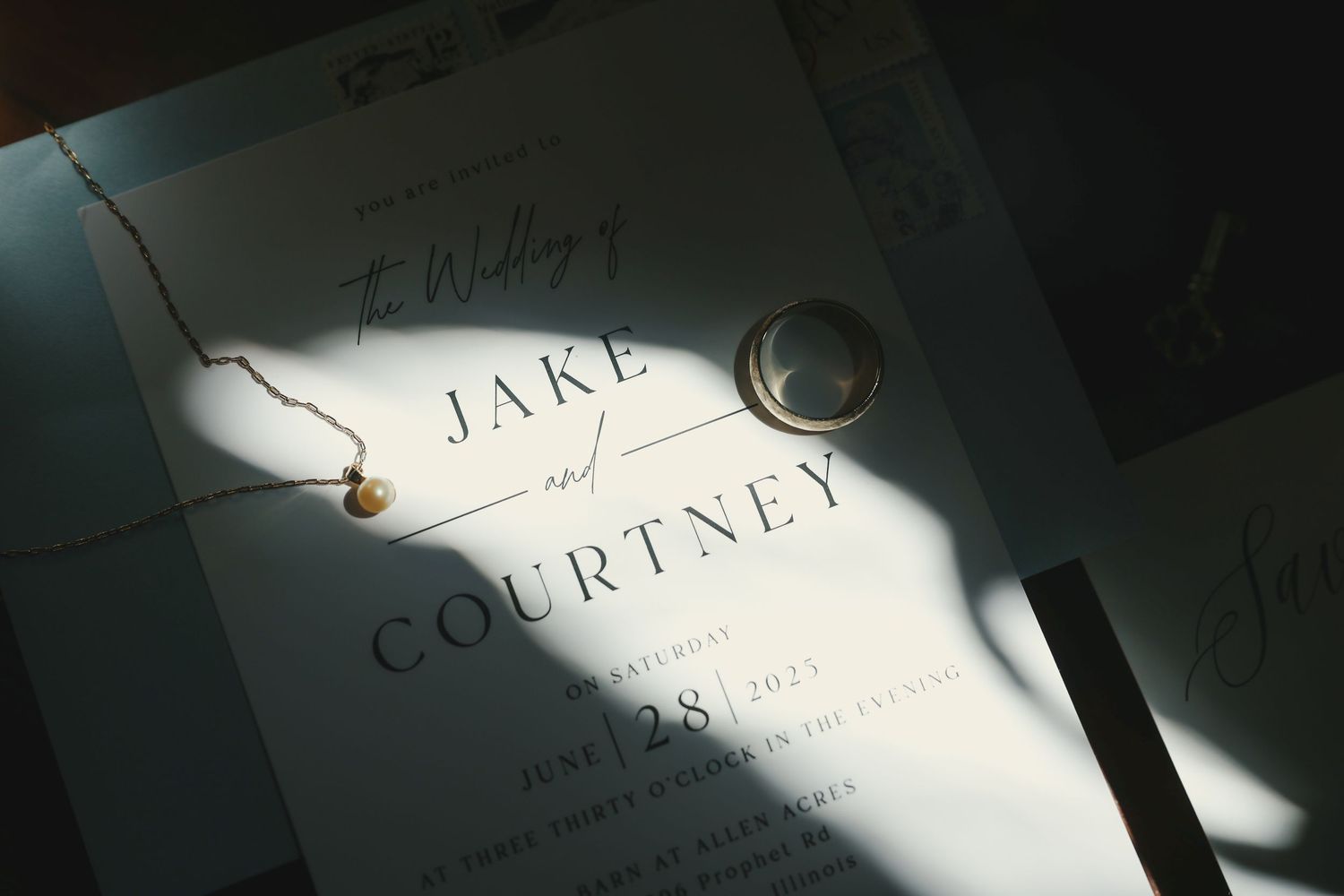 A wedding invitation with text and shadow patterns lies on a white surface in dramatic lighting.