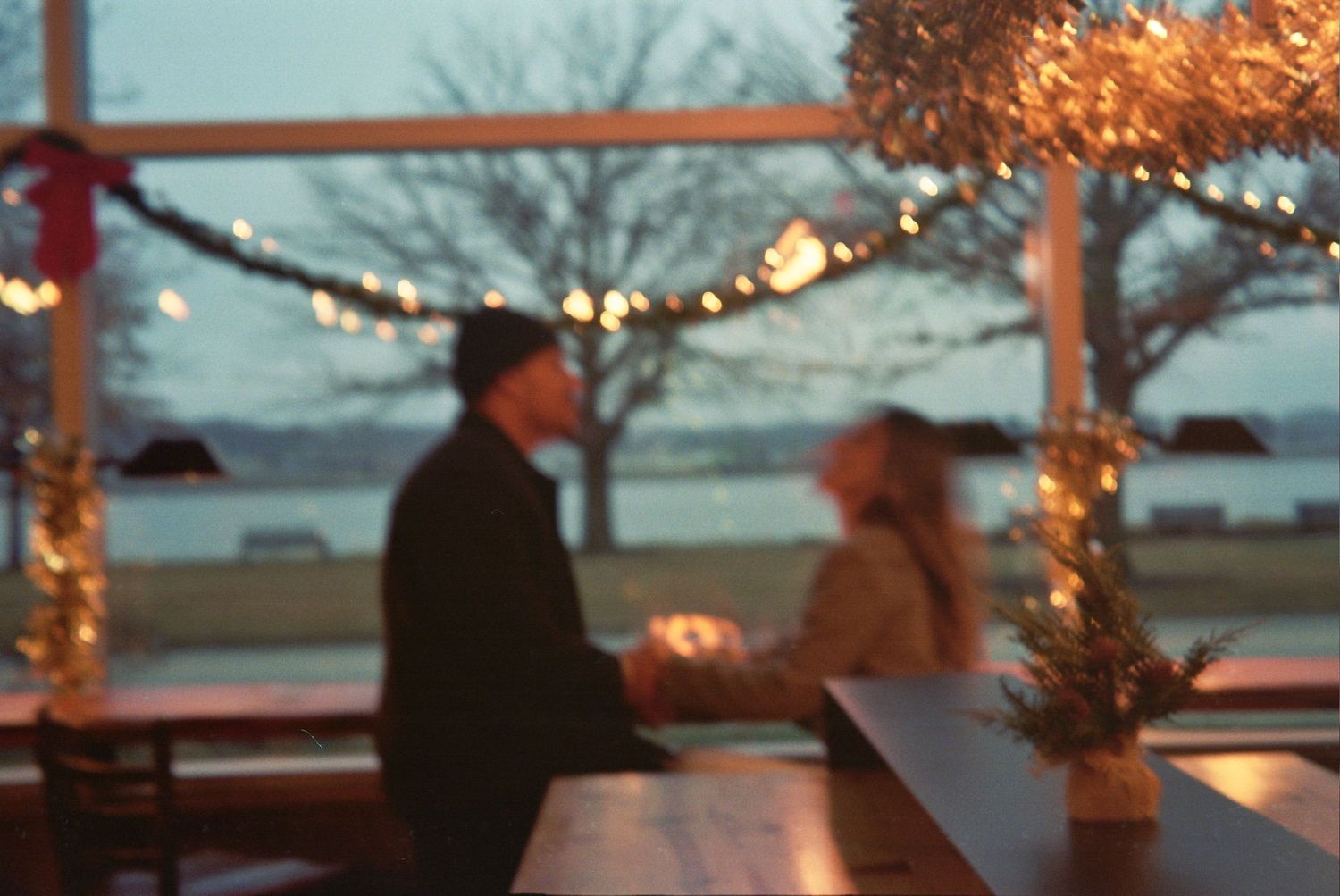 Outdoor winter wedding reception at dusk with string lights illuminating tables and trees in the snow.