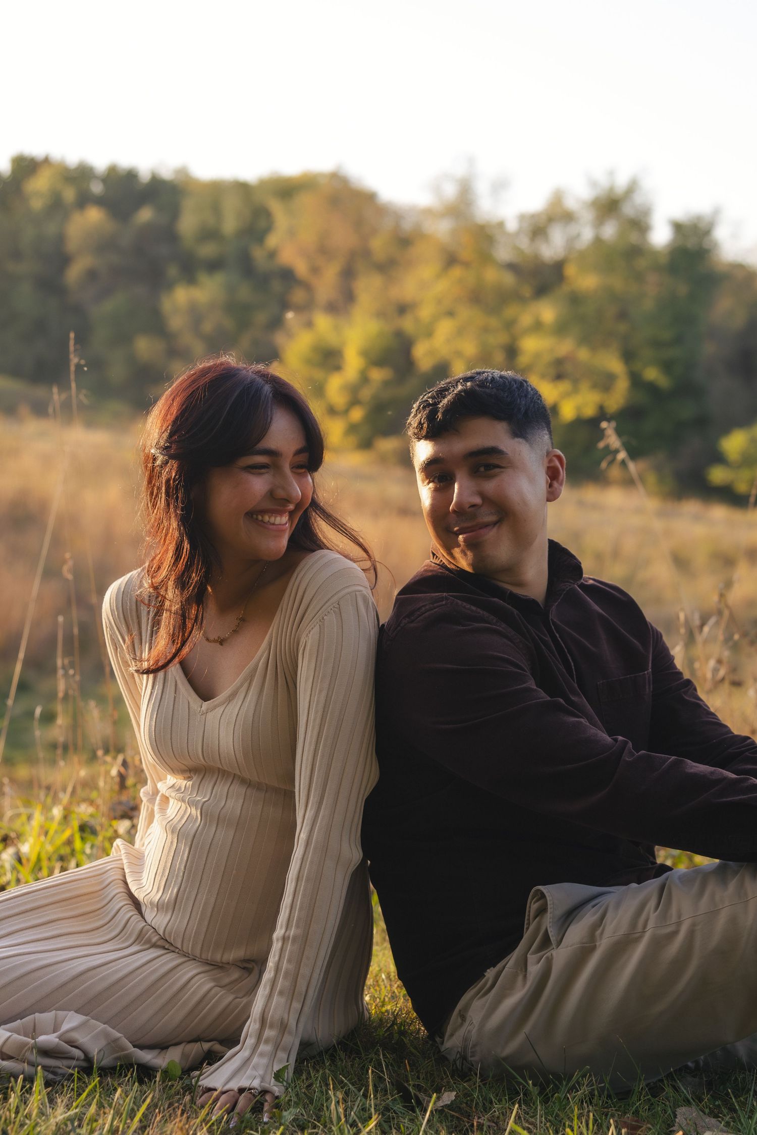 A couple lies in a grassy field during golden hour, sharing laughter and smiles in a series of candid moments.