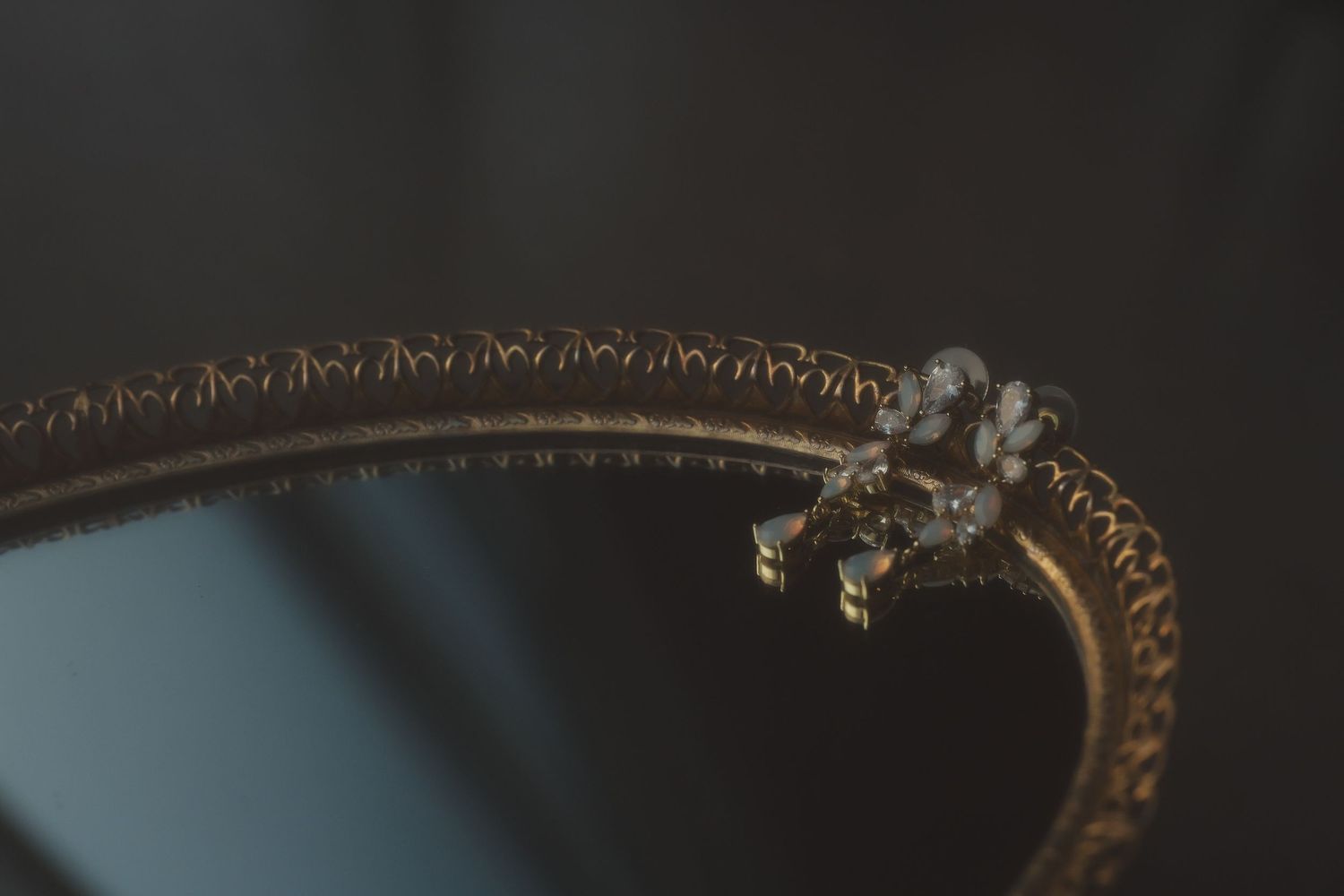 A tiny spider perched on the curved edge of an ornate metal frame or mirror against a dark background.