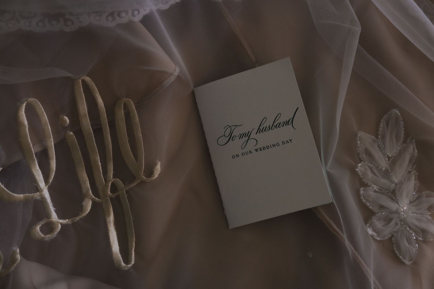 Wedding vow book reading 'To my husband on our wedding day' resting on bridal veil with floral details.