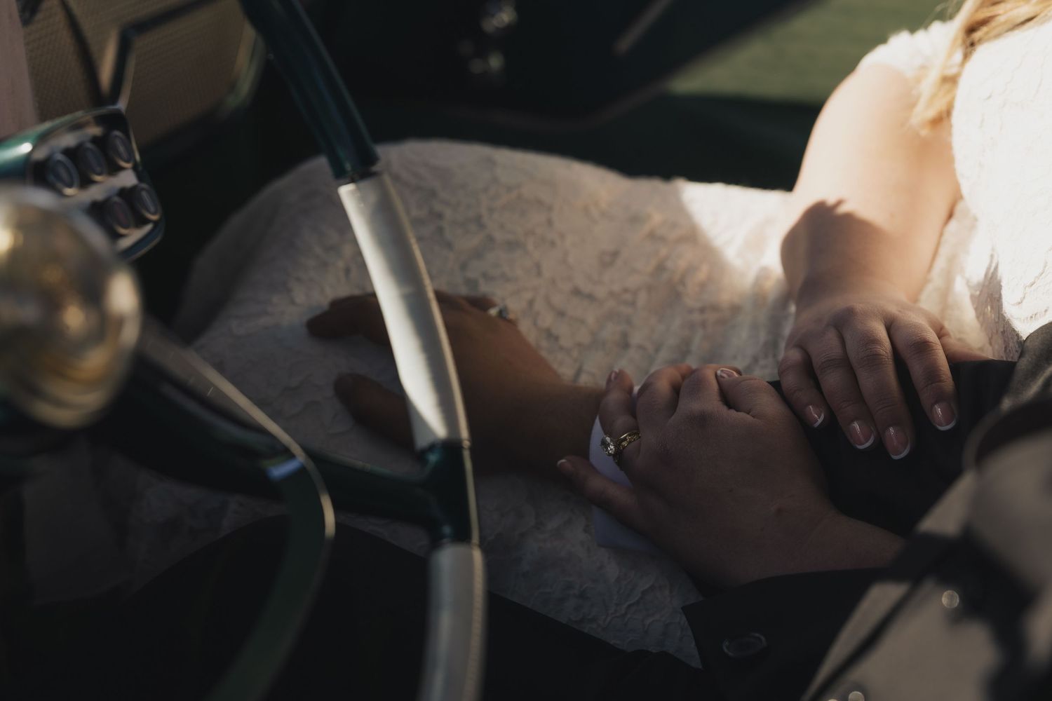 Close up view of hands resting on a steering wheel while driving a car in natural lighting.
