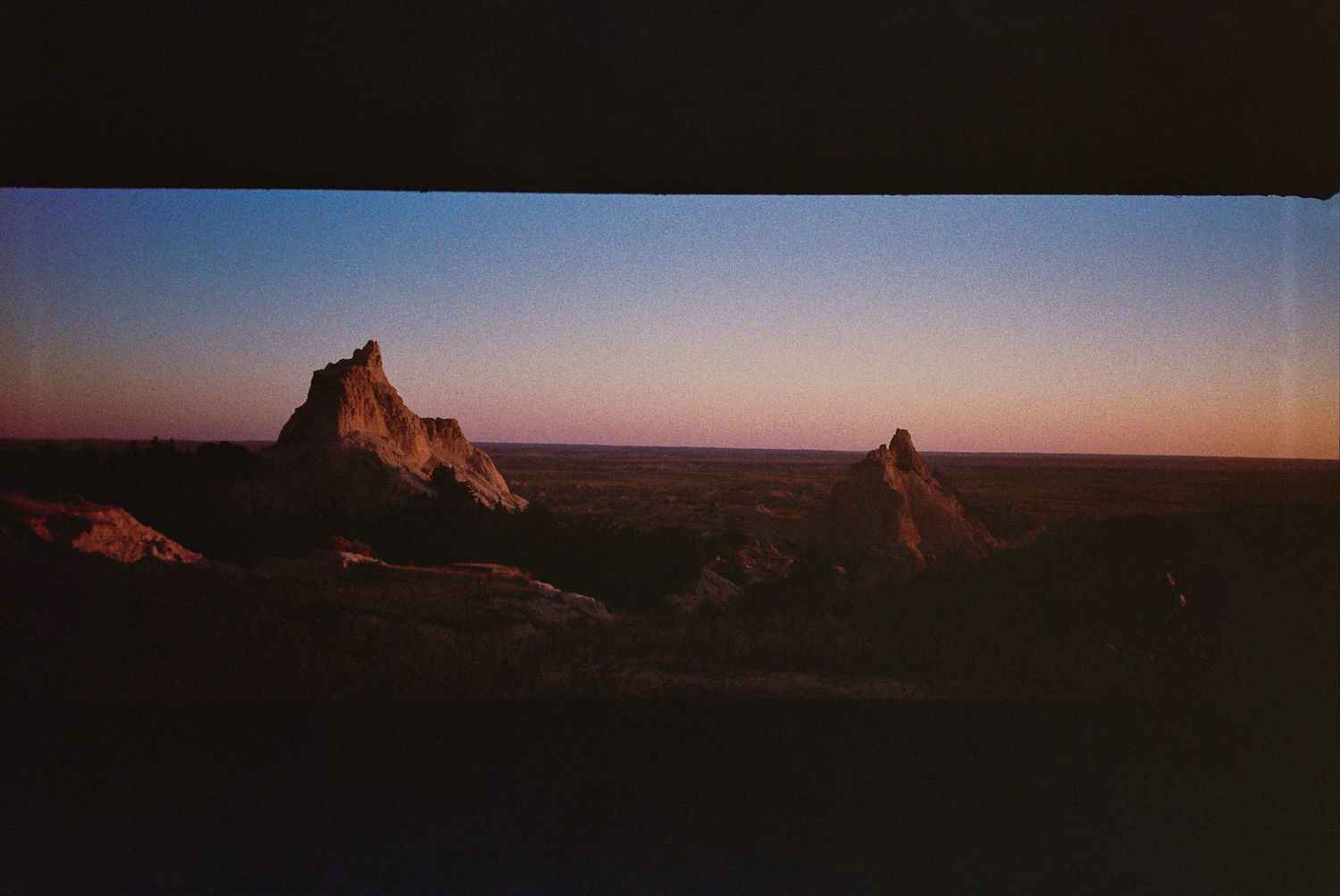 A scenic panoramic view of desert rock formations at sunset with warm golden light illuminating the landscape.