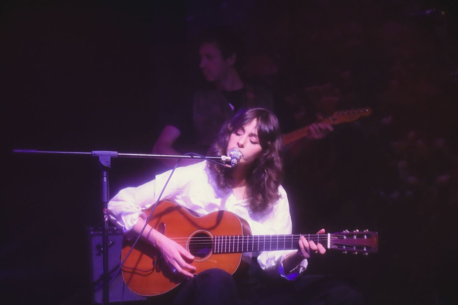 A musician performs passionately on an acoustic guitar under dramatic stage lighting during a concert.