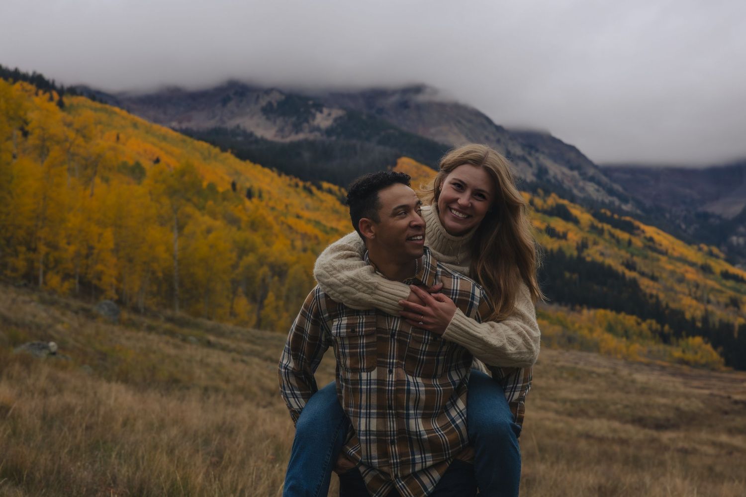 A couple embraces while enjoying a scenic mountain view with golden fall foliage in the background.