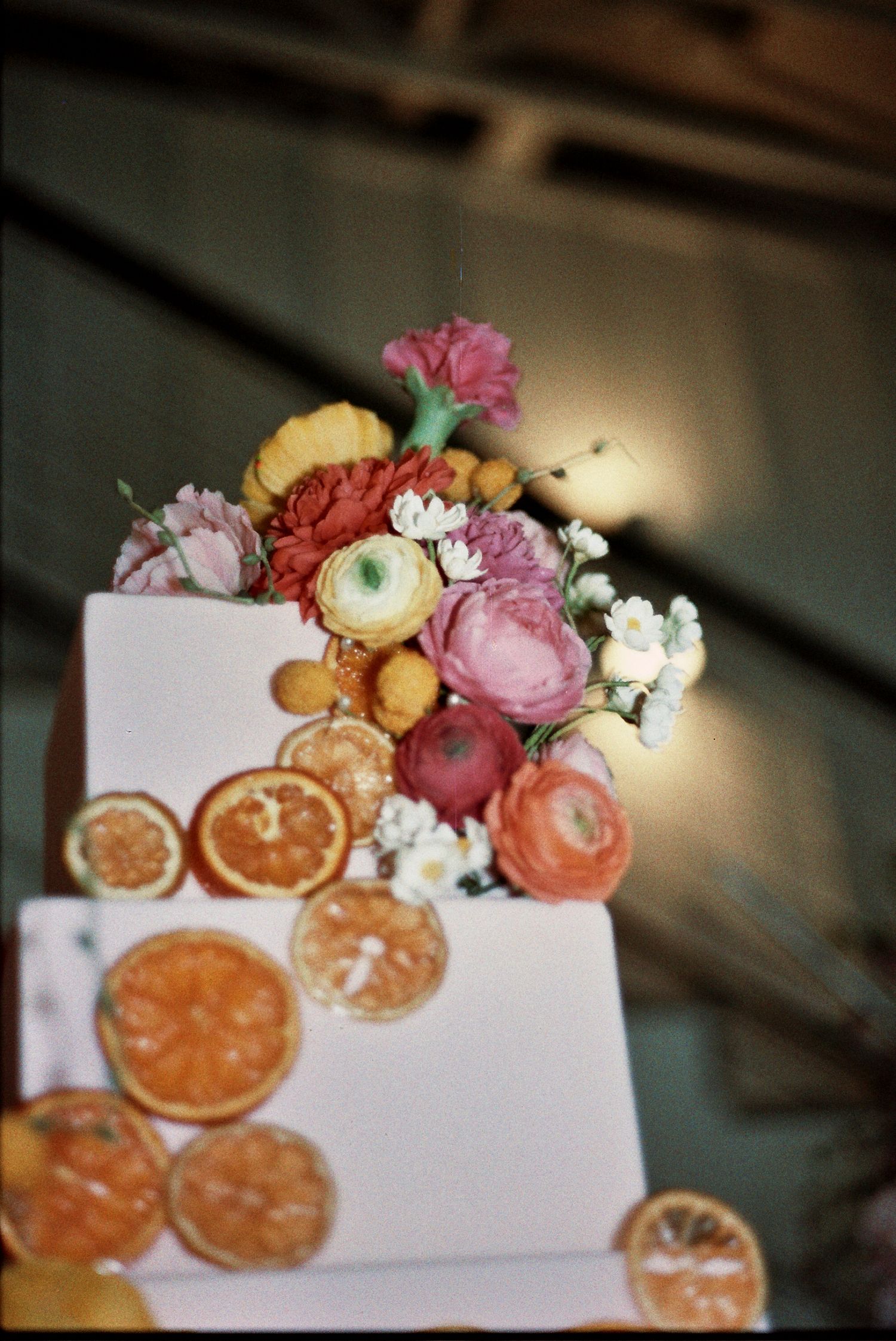 Elegant white wedding cake decorated with dried orange slices and fresh pink flowers in a rustic setting.
