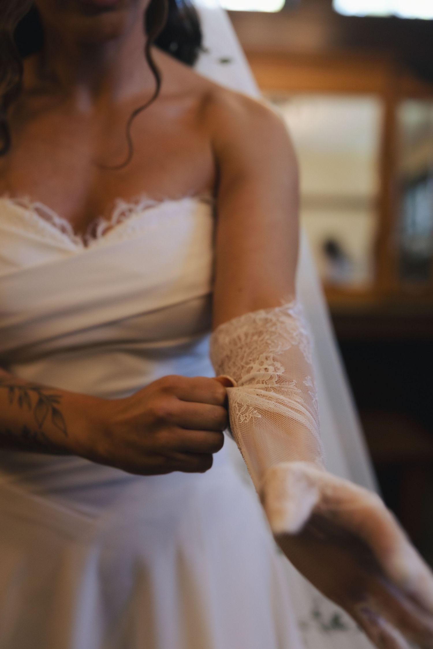 Bride in white strapless lace wedding dress adjusting her lace sleeve glove, with a floral tattoo on her arm.