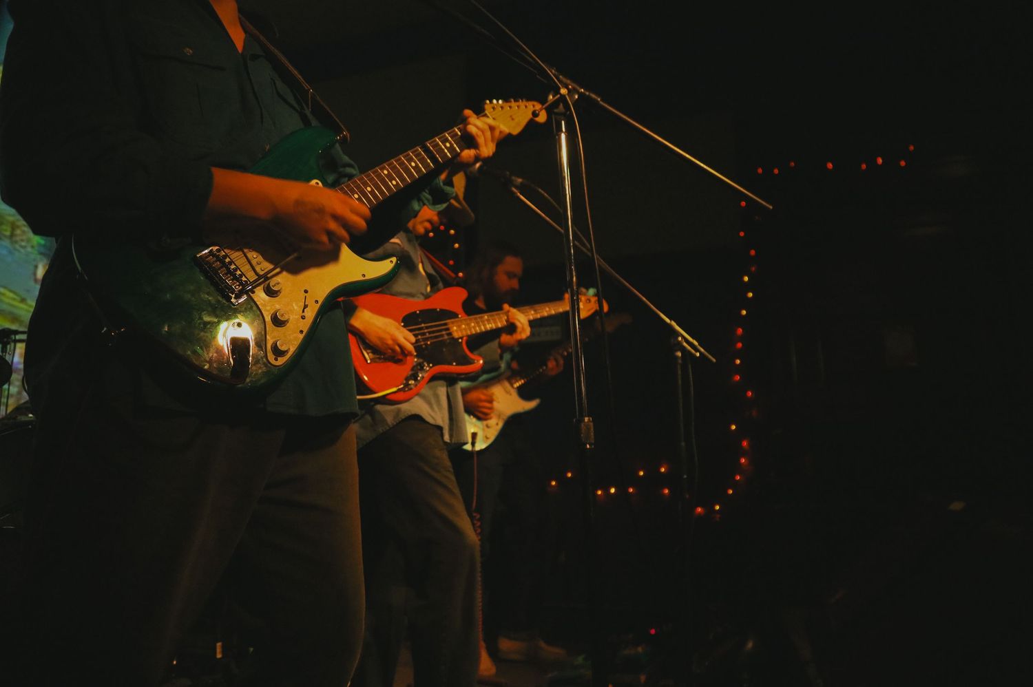 Electric guitar player performs on dimly lit stage during live music performance.