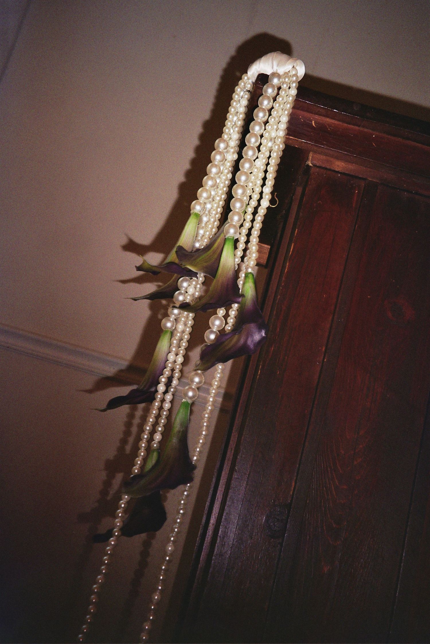 A green parrot perches on a dark wooden wardrobe next to hanging crystal beads in a dimly lit room.