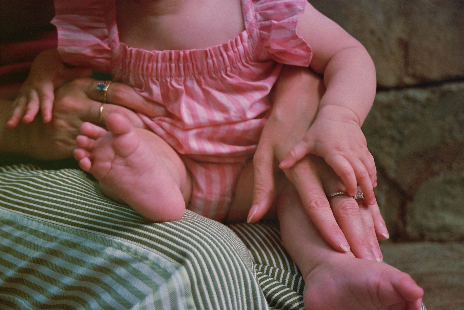 A baby in a pink dress sitting on an adult's lap, showing chubby legs and tiny feet with adult hands visible.