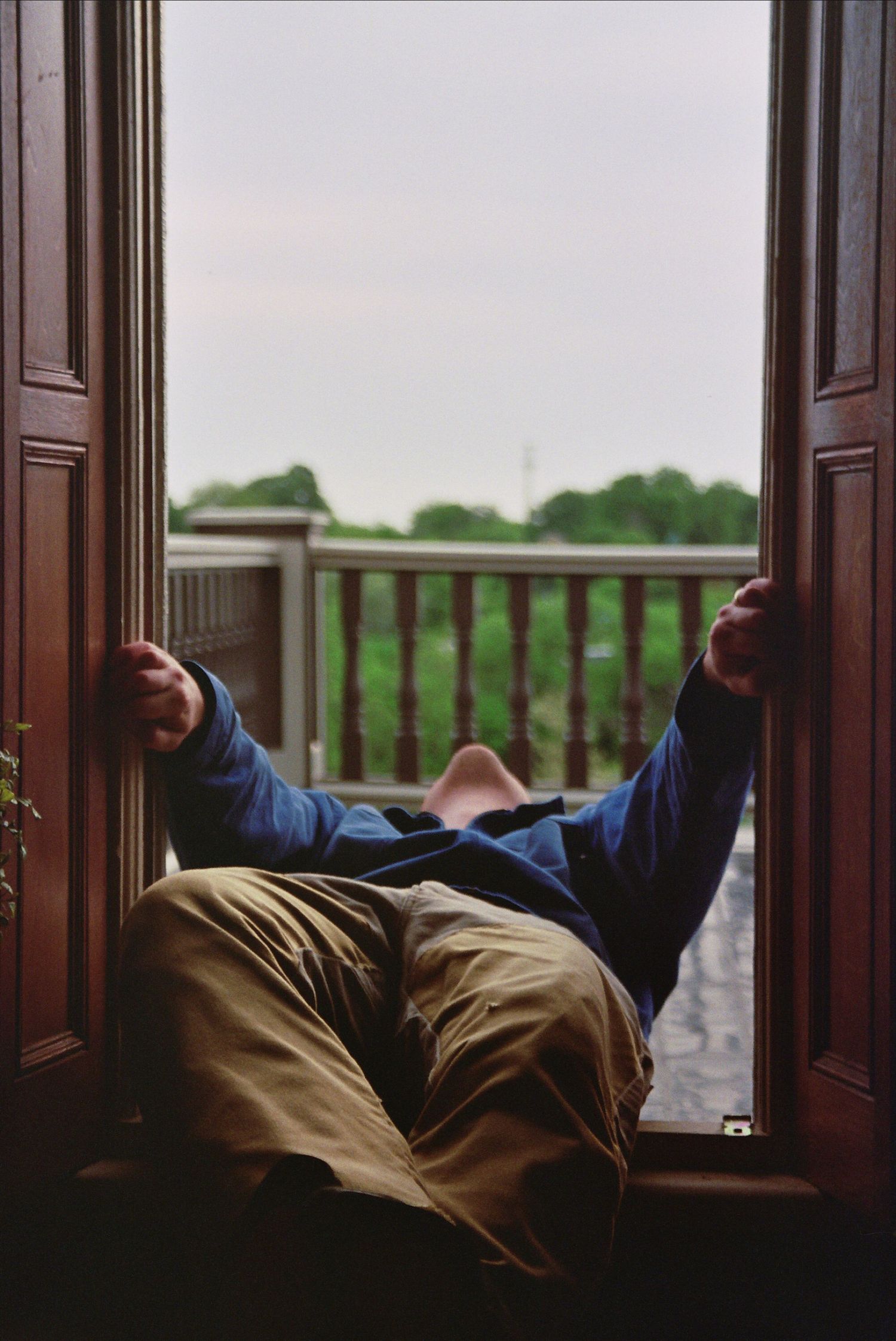 Person in blue jacket and khaki pants lying in open doorway overlooking a green outdoor deck and trees.