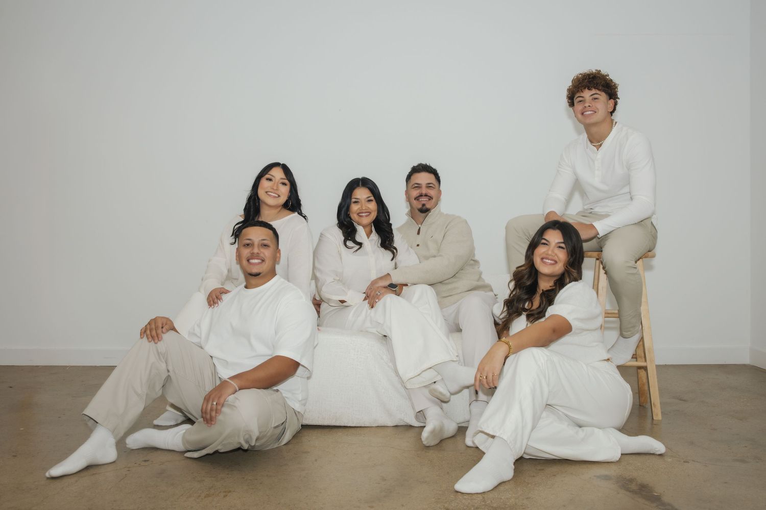 Six people in matching white outfits pose together for a family portrait against a white studio background.