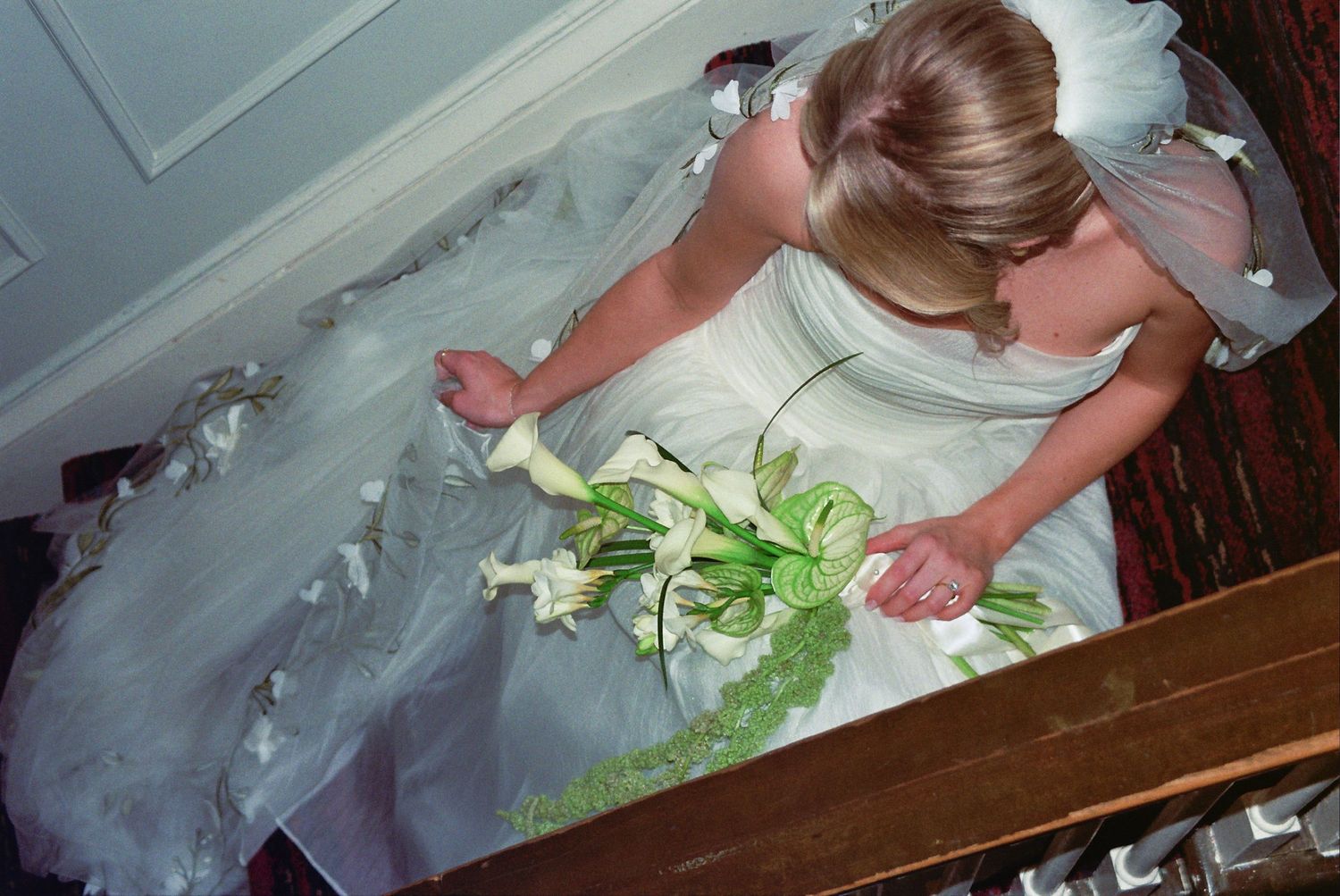 Bride in white wedding gown holding green and white bouquet, photographed from above on staircase.