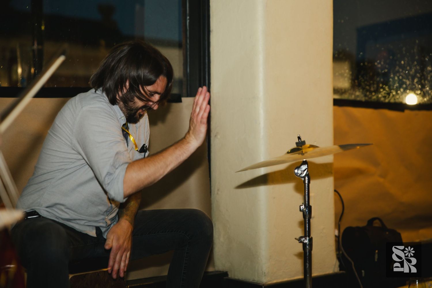 Musical performers play instruments against a cream-colored wall in an indoor venue.