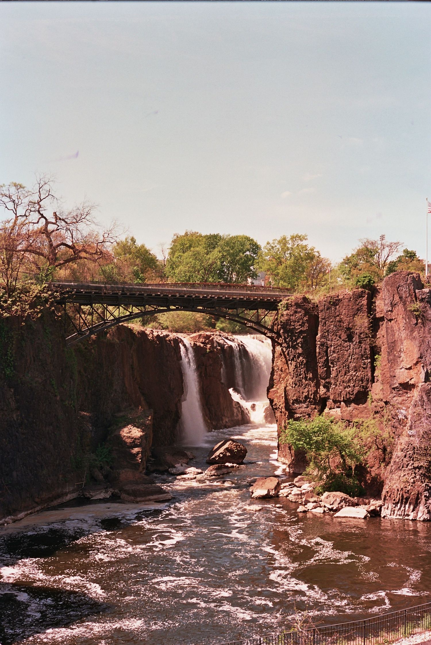 A scenic waterfall cascades over rocky cliffs beneath a bridge in a natural landscape with lush greenery.