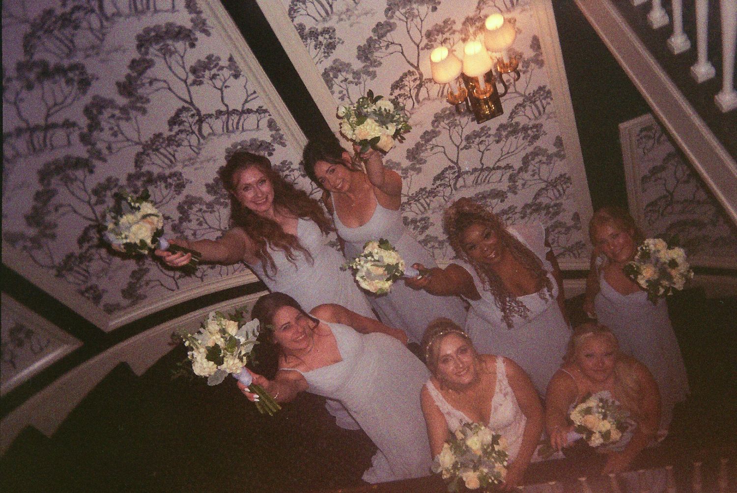 A group gathers on floral-patterned furniture in a dimly lit room with warm lighting and decorative elements.