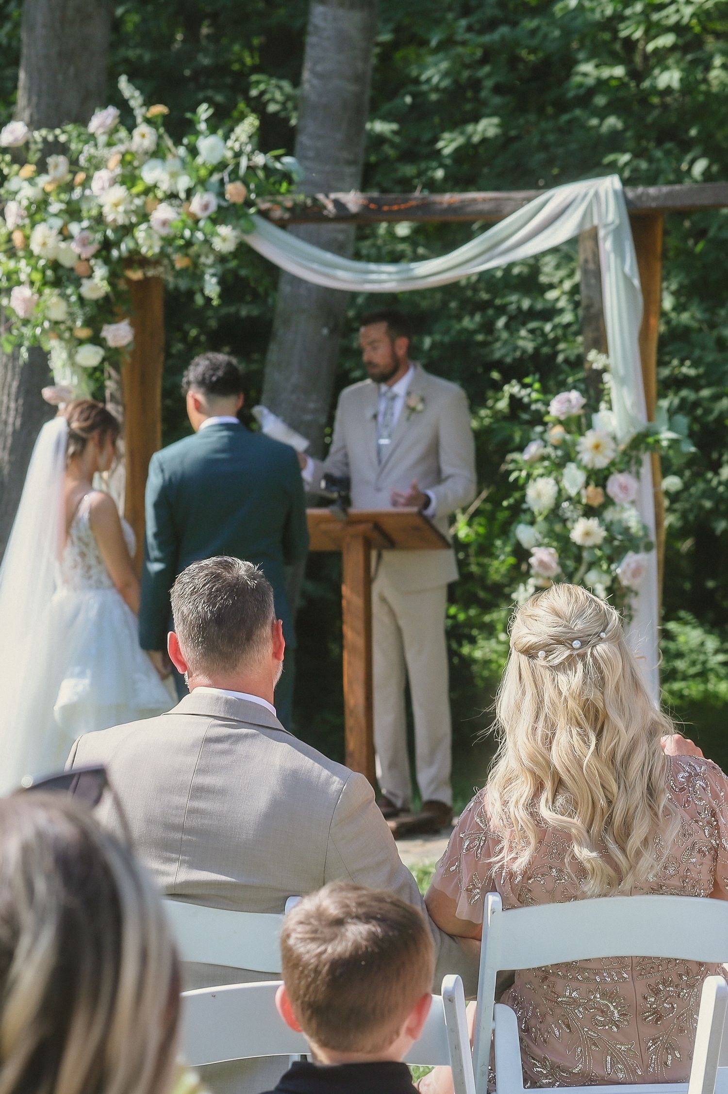 Outdoor wedding ceremony under draped arch with white floral decorations.