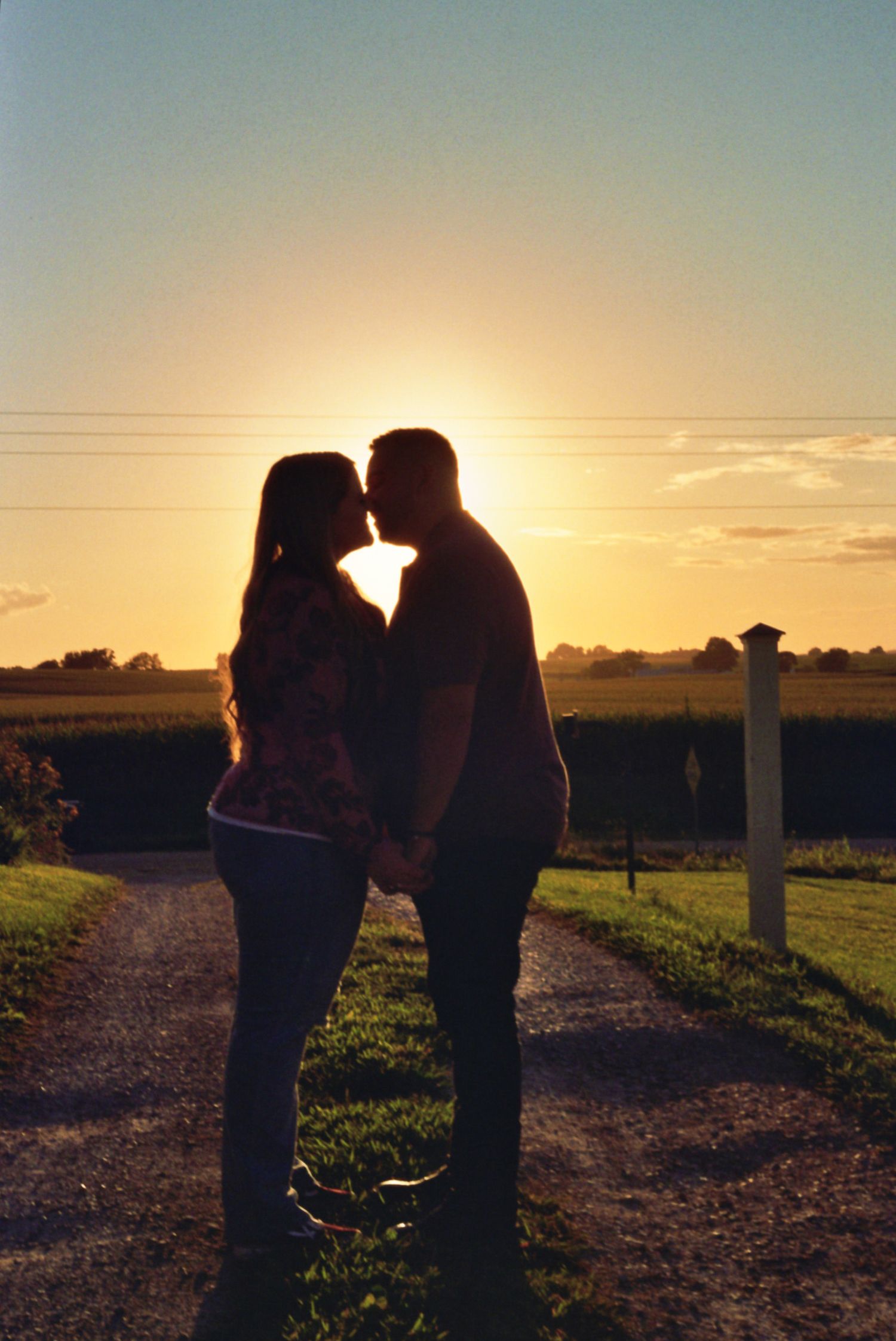 Silhouetted couple sharing a tender moment on a country path at sunset against a glowing golden sky.