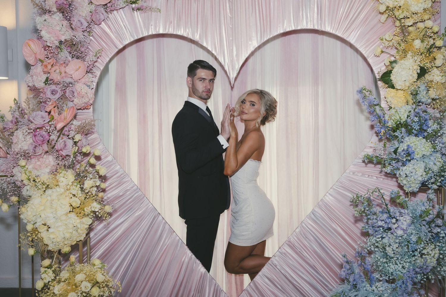 A couple shares multiple romantic moments in front of a shimmering backdrop adorned with pastel floral arrangements.