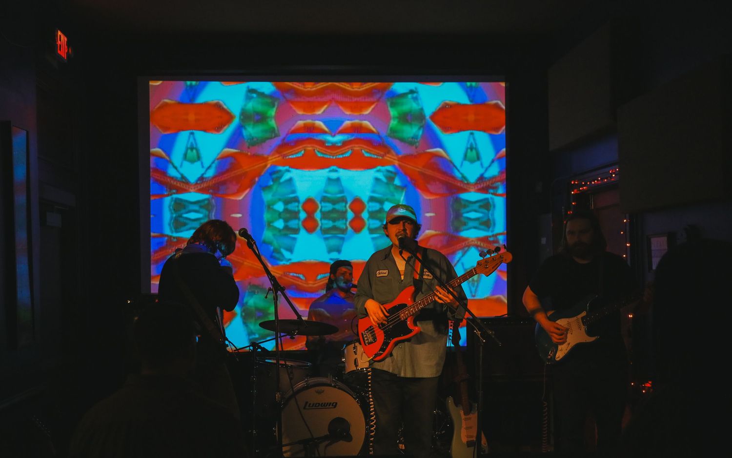 Performers on stage with vibrant blue and orange digital backdrop displays during a live music performance.