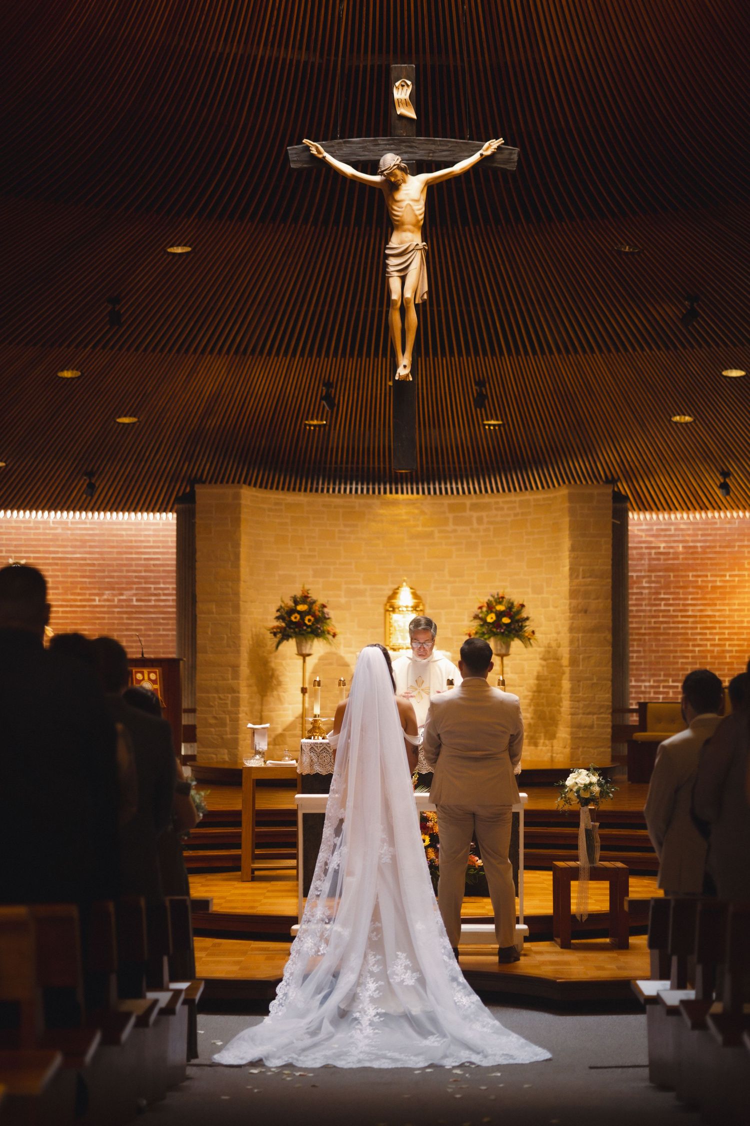 A bride and groom stand at a church altar beneath a large crucifix during their wedding ceremony.