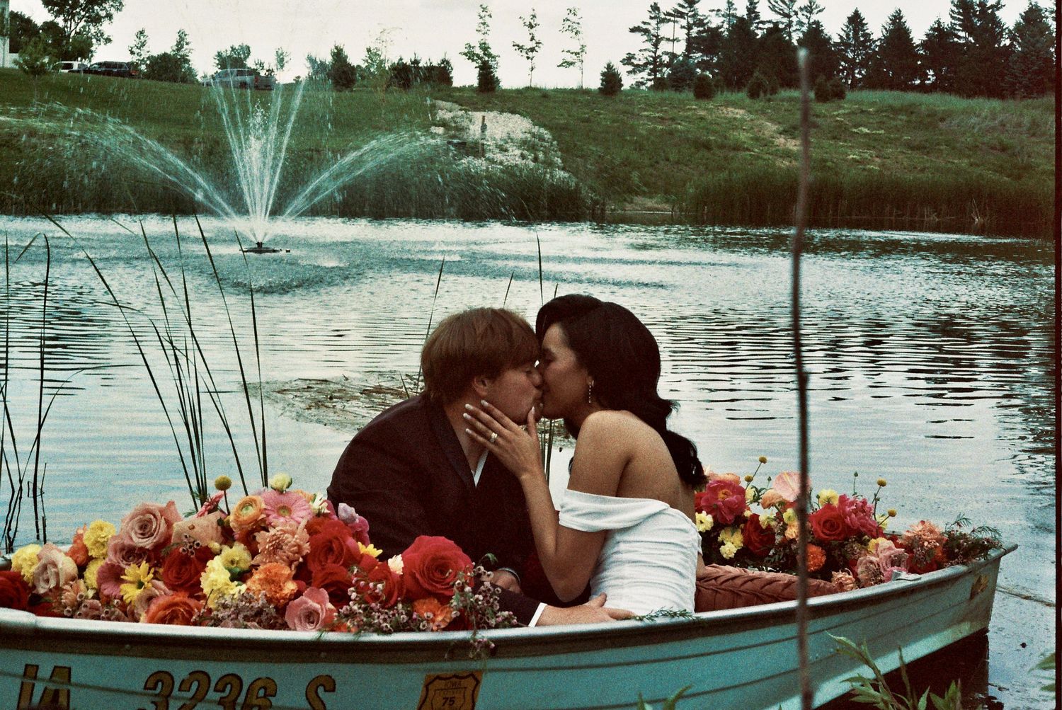 A romantic scene in a boat filled with red flowers as a fountain sprays water over a tranquil lake.
