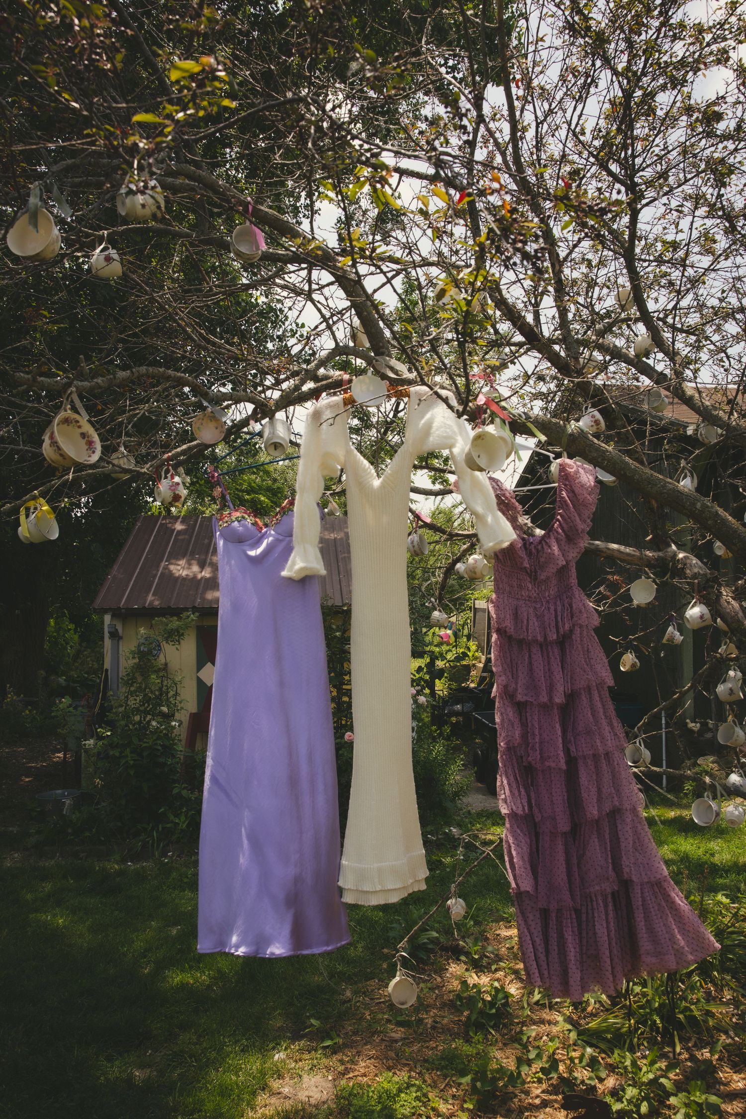 Three vintage-style dresses hanging on a clothesline outdoors against a backdrop of trees and foliage in natural light.