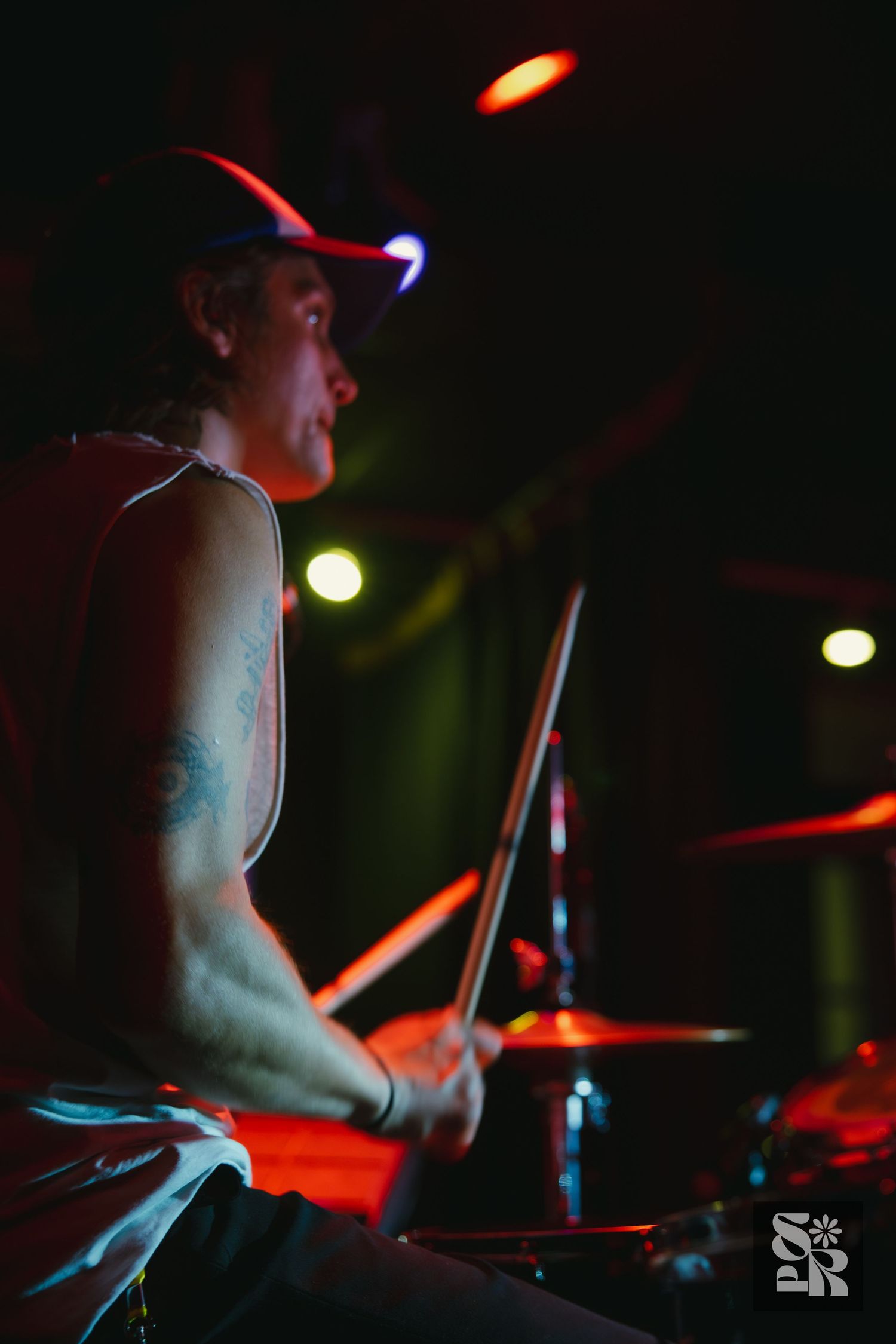Silhouetted drummer performing on stage with dramatic red and blue lighting effects.