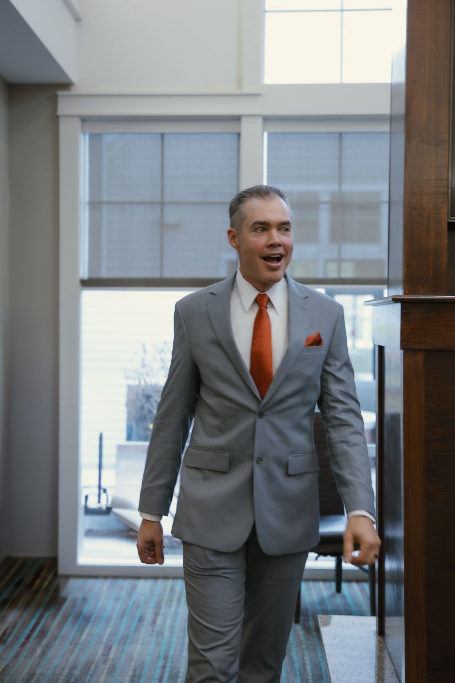Person in gray suit and orange tie walking through modern office hallway.