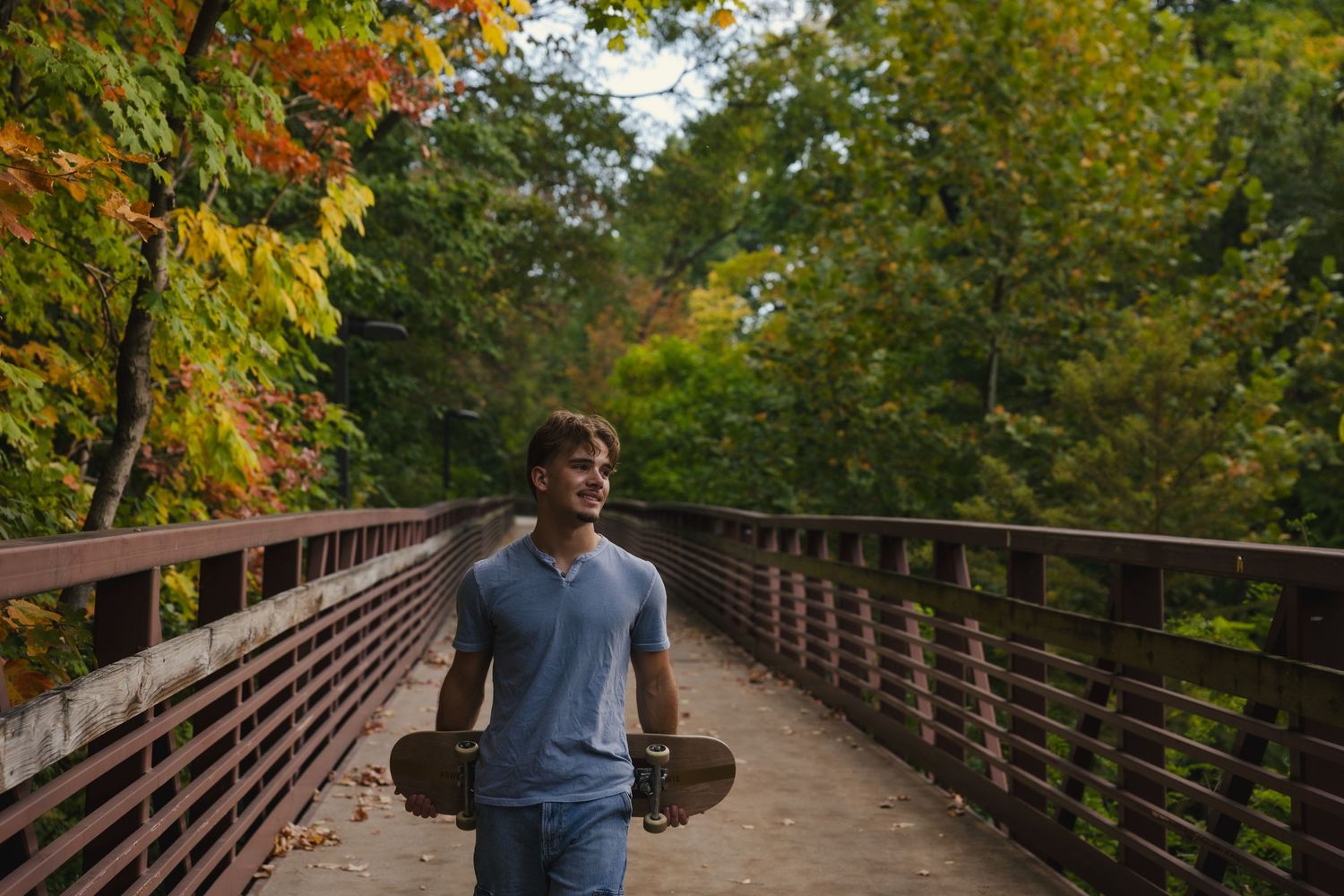 A wooden boardwalk path winds through autumn trees with golden foliage in a peaceful forest setting.