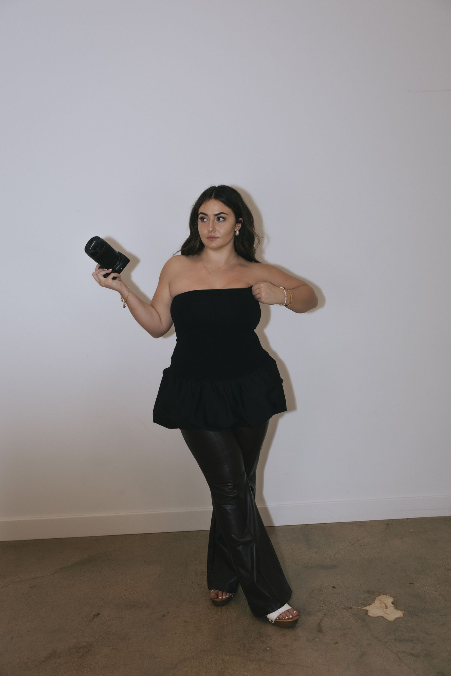 A person in a flowing black dress poses dramatically against a white wall in a series of artistic movements.