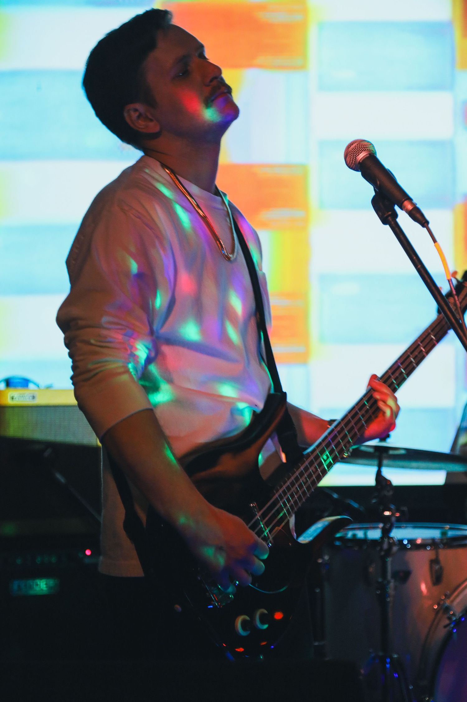 Bass guitarist performs on stage illuminated by colorful spotlights and disco effects during live music performance.