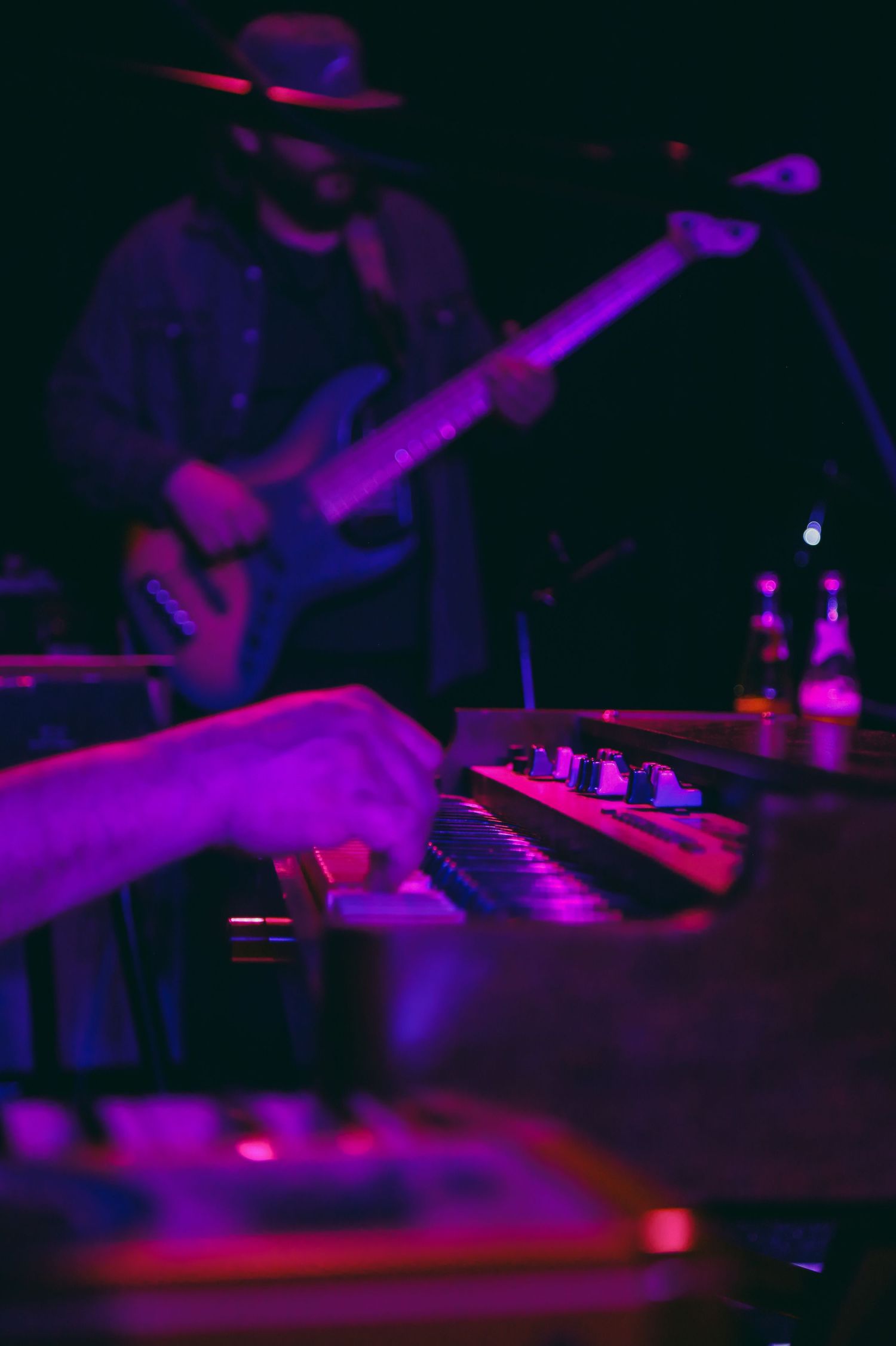 Close-up view of a DJ mixer board illuminated by purple and red stage lighting during a nightclub performance.