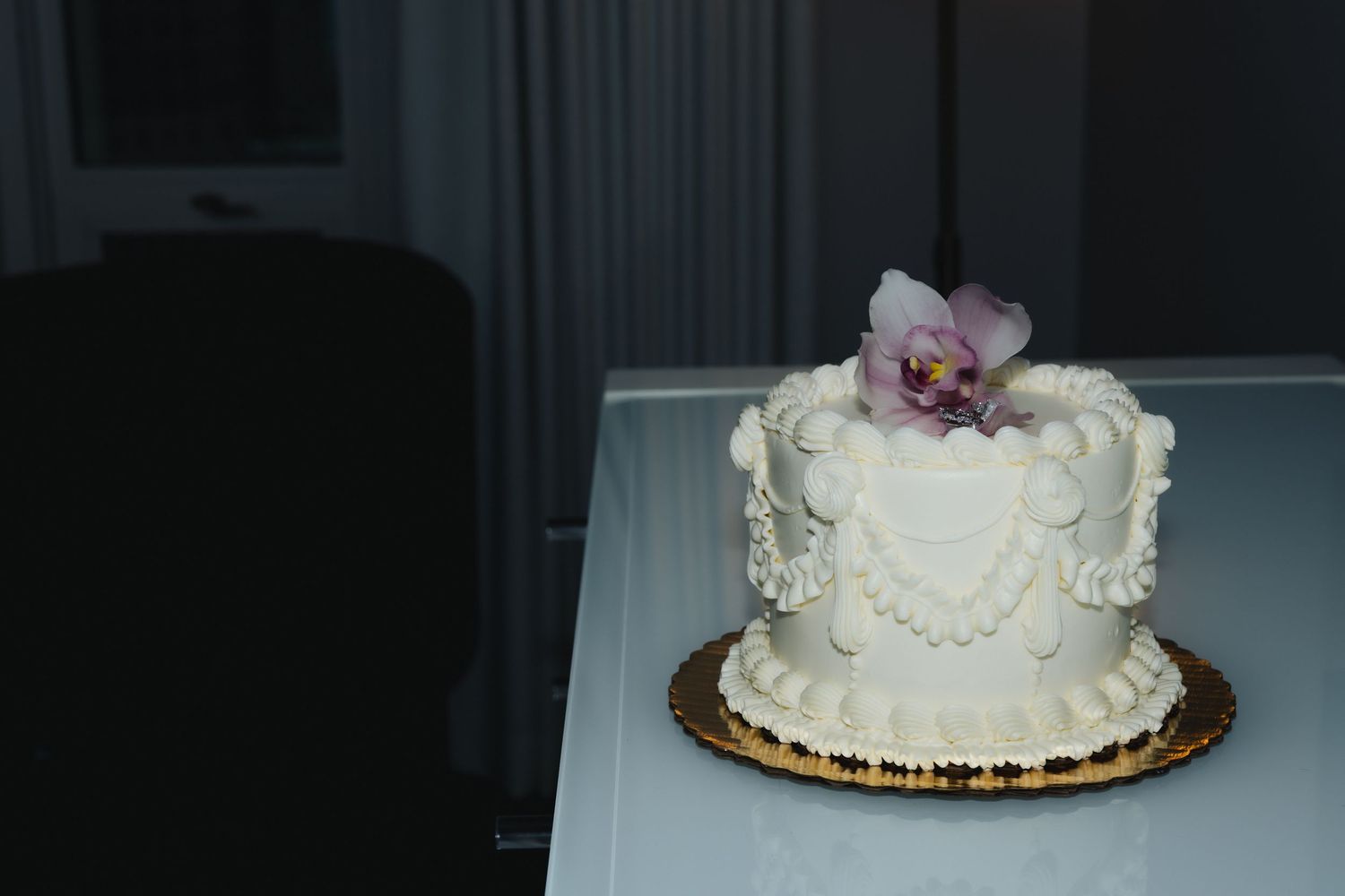 White wedding cake decorated with pale pink roses and floral accents on a dark table during an evening reception.