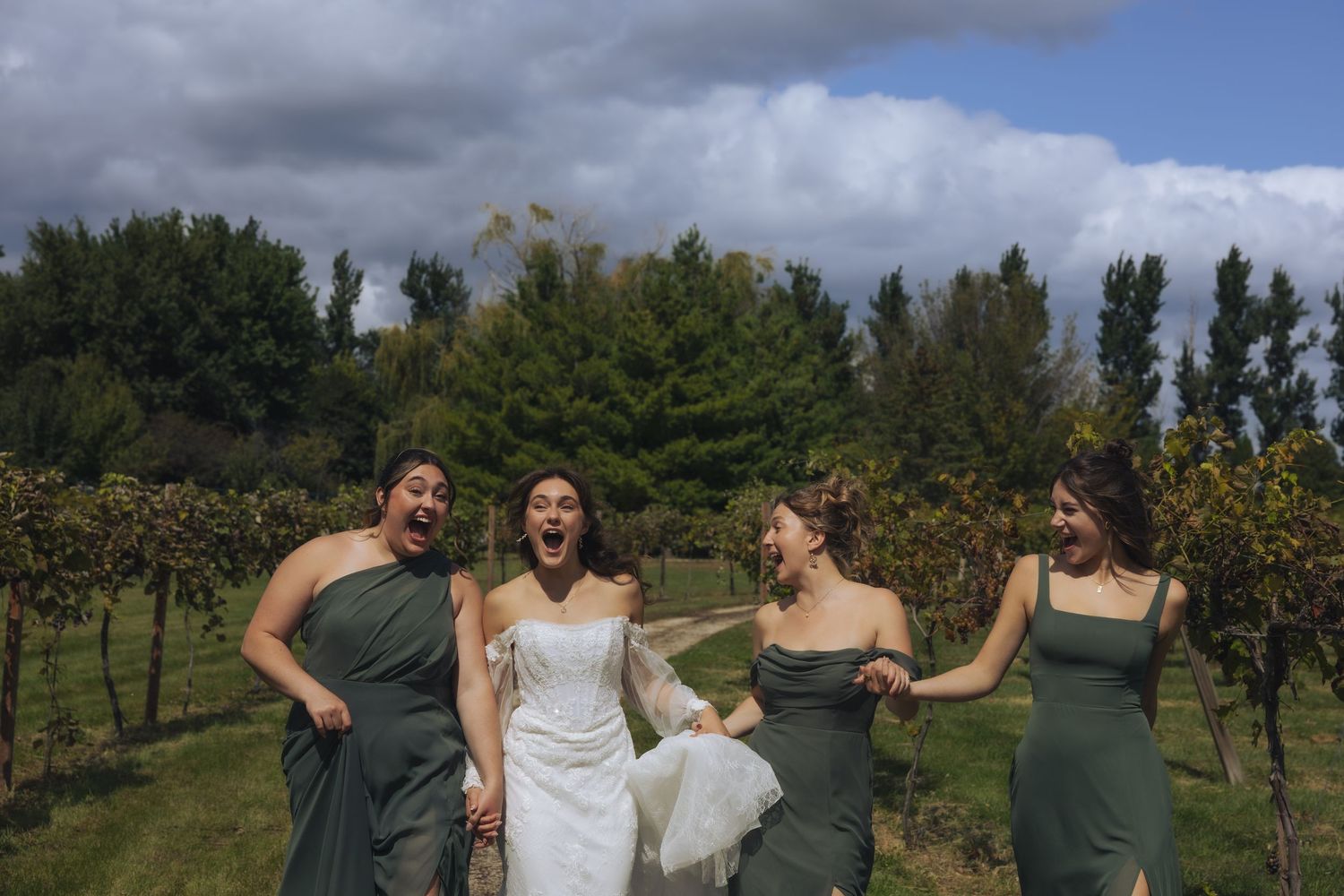 Wedding party dancing and celebrating in a scenic vineyard setting during sunset hours.