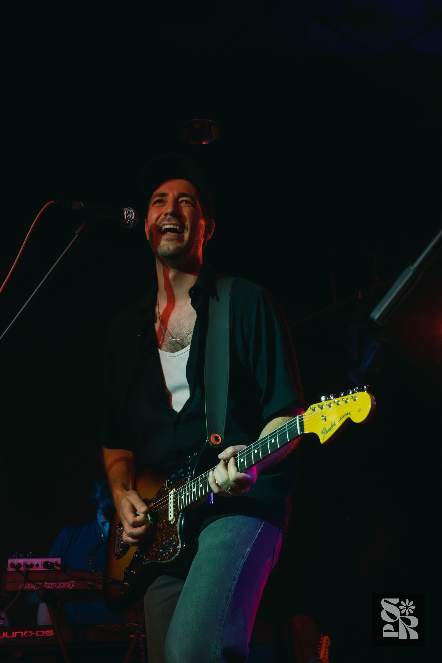 Musician performs on stage with an electric guitar in dramatic lighting with blue and red tones during live concert.