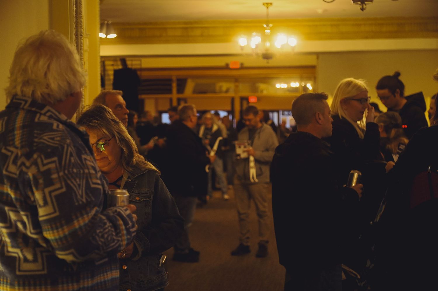 The golden-lit interior of a ballroom shows elegantly dressed guests mingling at a formal evening event.