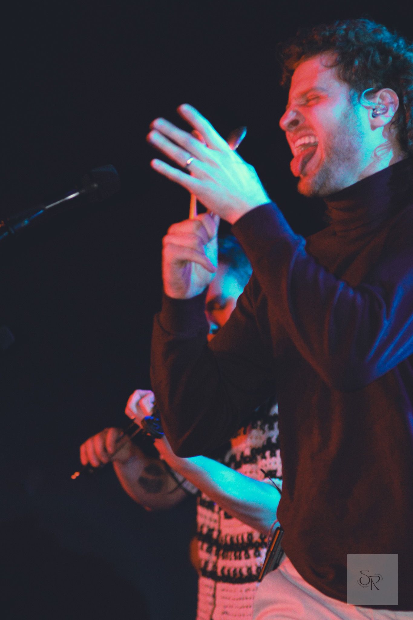 A performer singing passionately on stage illuminated by red and blue lighting during a live concert performance.