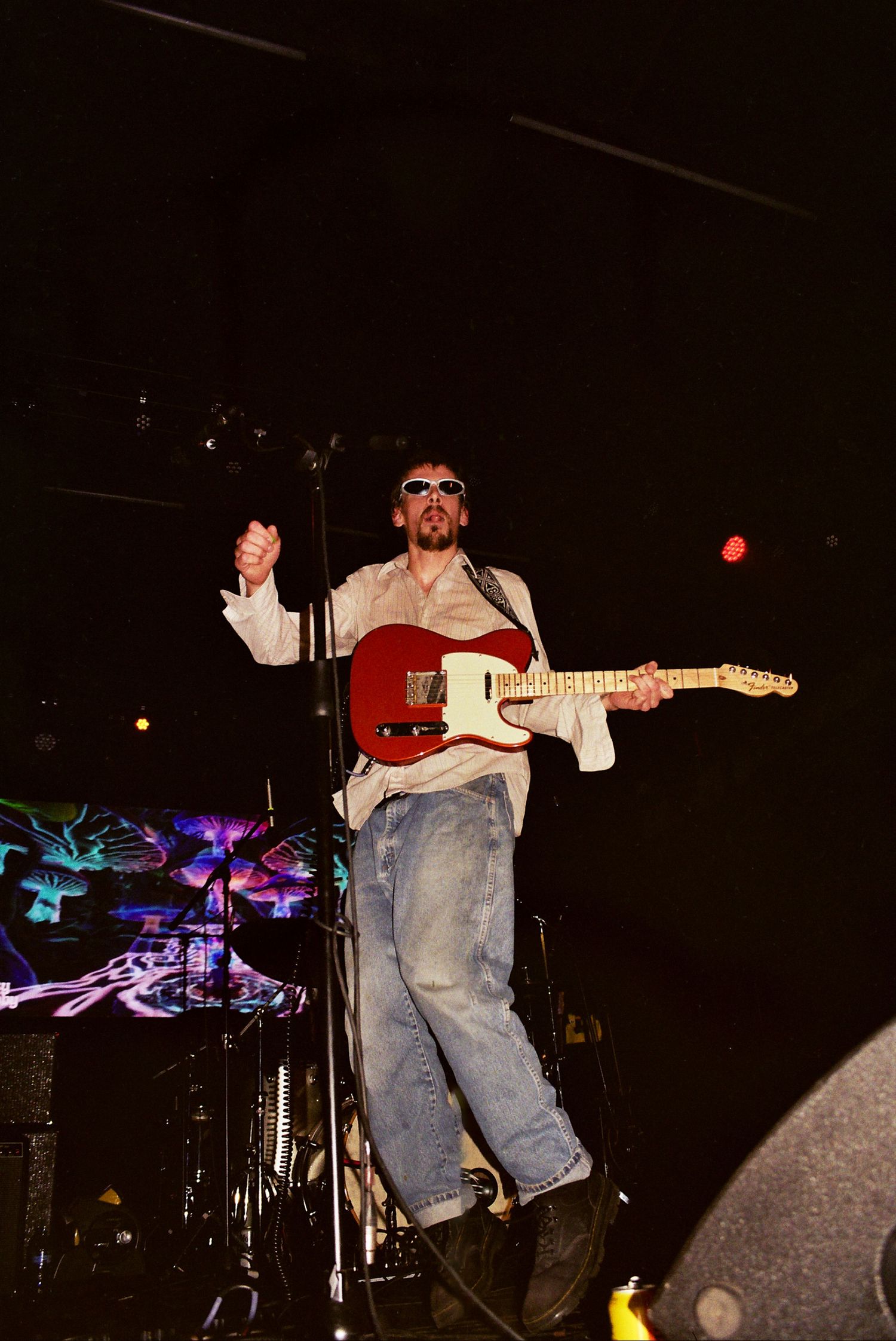 Performer in casual attire playing a red electric guitar on stage during a live concert.